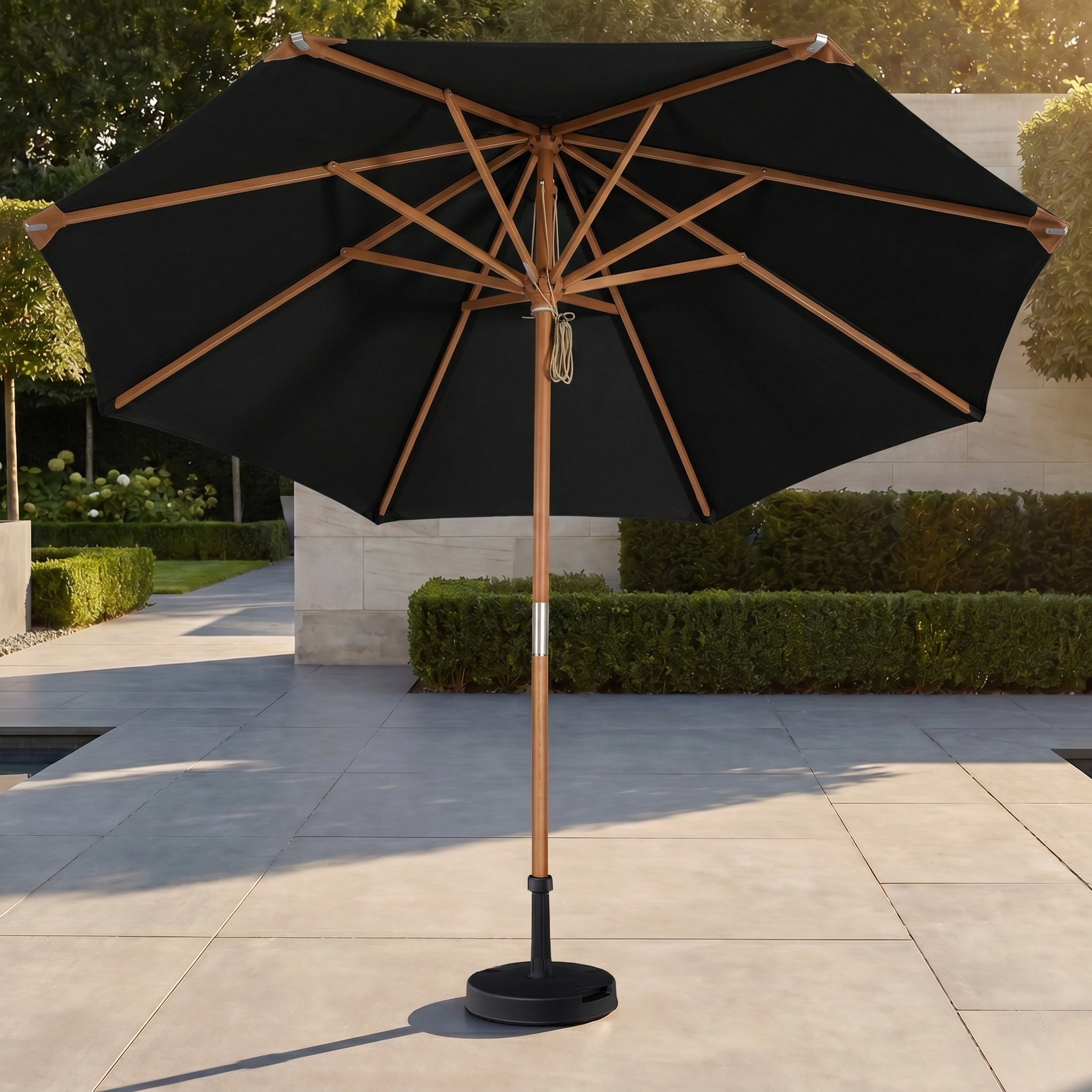 The Styx 3m Round Deluxe Wooden Parasol in Black stands on a stone patio in a landscaped garden, providing stylish shade and UV protection.