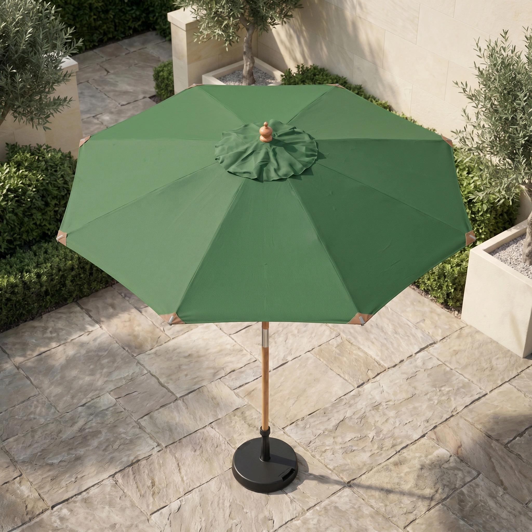 The Styx 3m Round Deluxe Wooden Parasol in Green stands on a stone-tiled terrace, surrounded by planters filled with greenery and small trees.