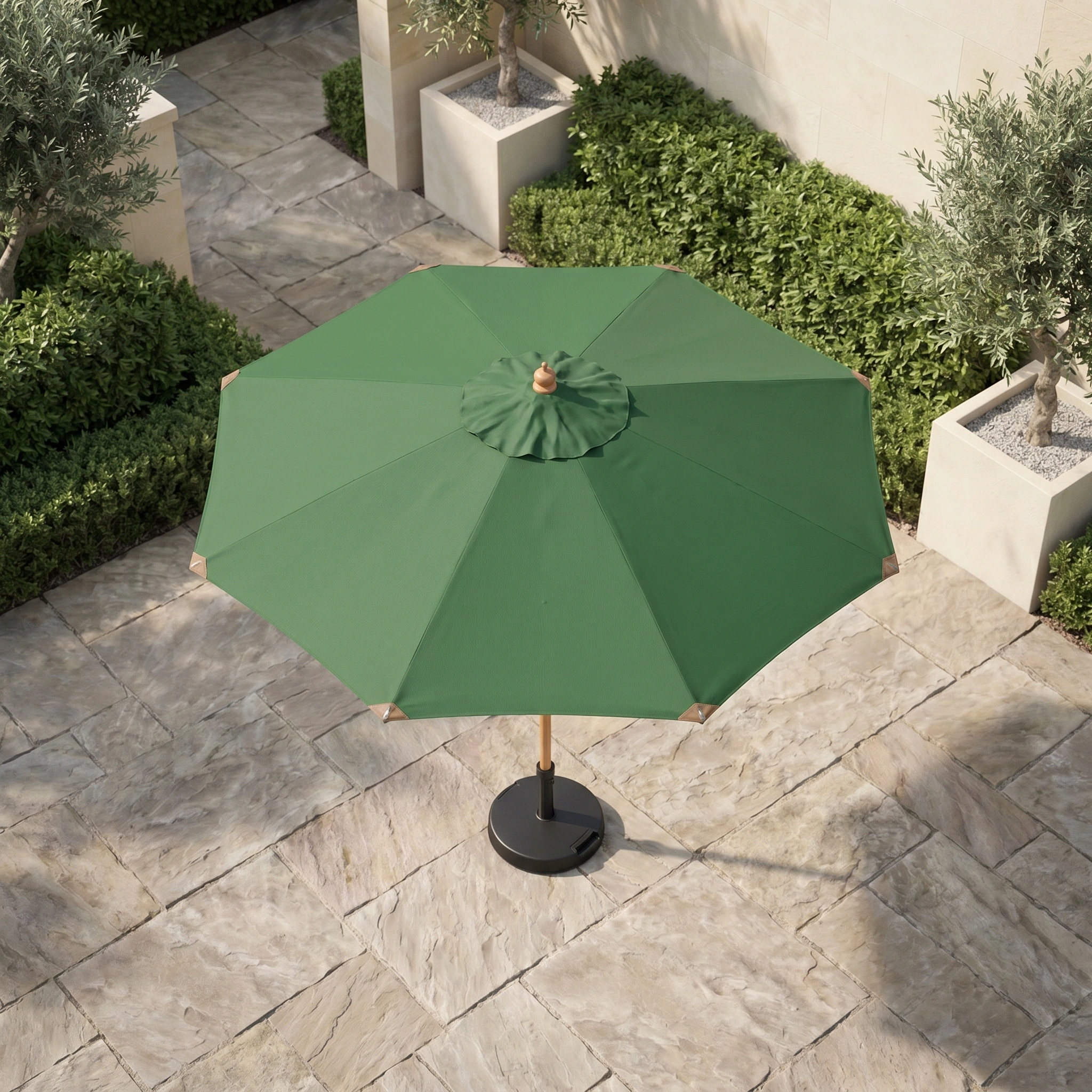 Styx 3m Round Deluxe Wooden Parasol in Green on a stone-tiled terrace, surrounded by hedges and potted plants, viewed from above.