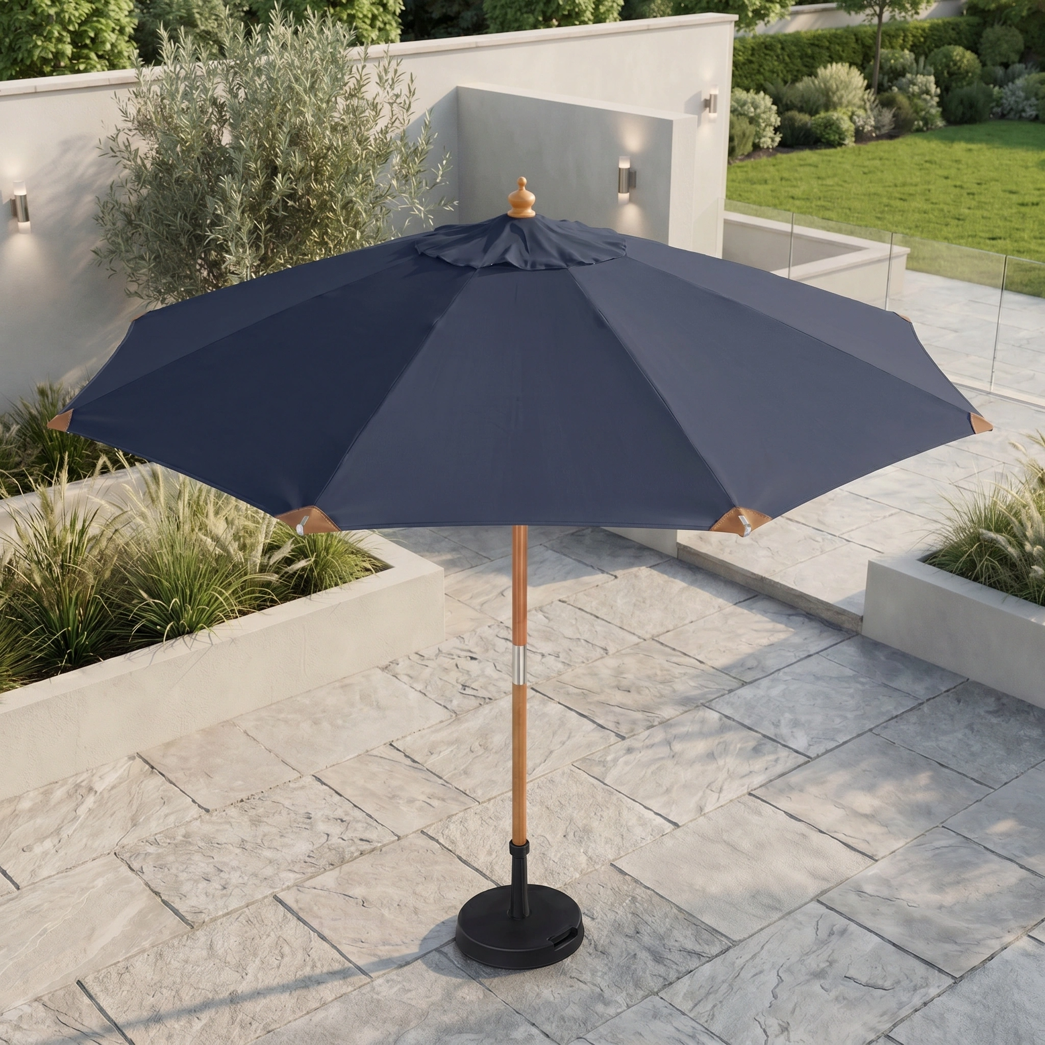 A Styx 3m Round Deluxe Wooden Parasol in Navy stands on a stone-tiled terrace, with greenery and lawn visible in the background.