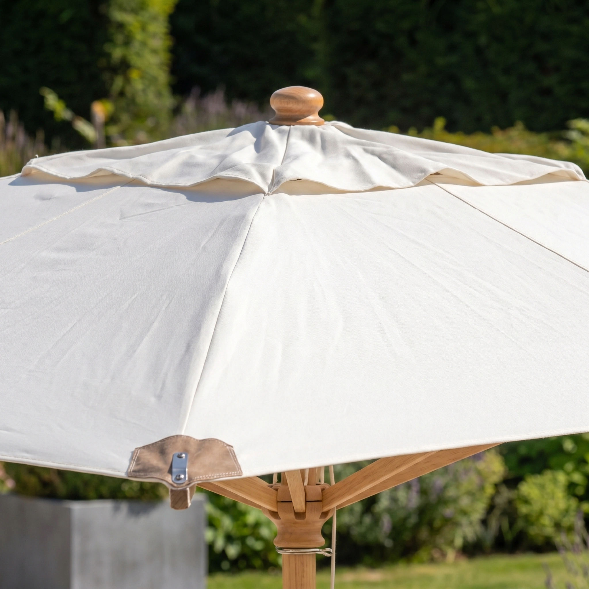 The Styx 3m x 2m Rectangular Deluxe Wooden Parasol in Beige stands outdoors in a garden, its sturdy wooden pole and neutral shade complementing the lush greenery around it.