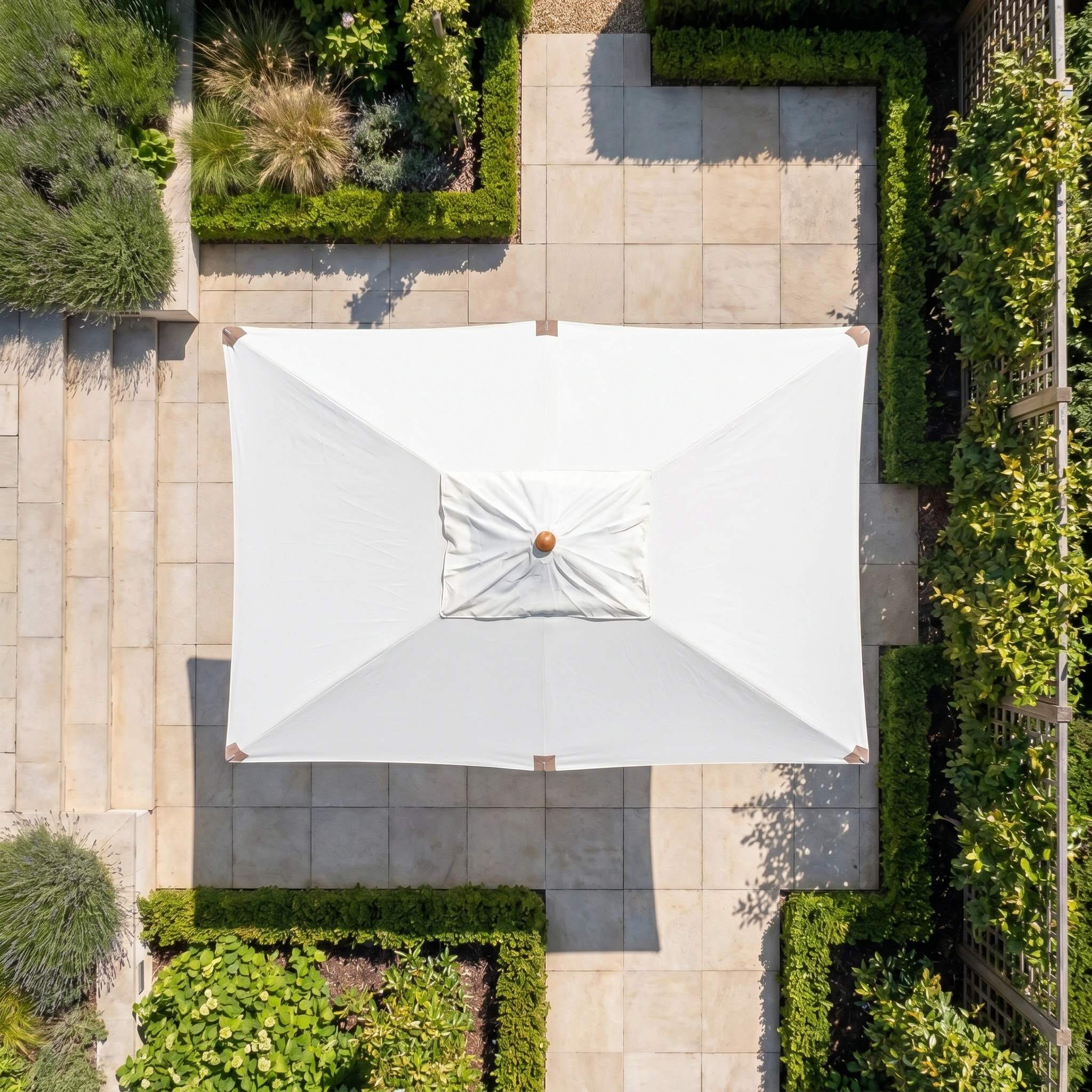 The Styx 3m x 2m Rectangular Deluxe Wooden Parasol in Beige is seen from above, centered in a landscaped garden featuring stone paths and green hedges.
