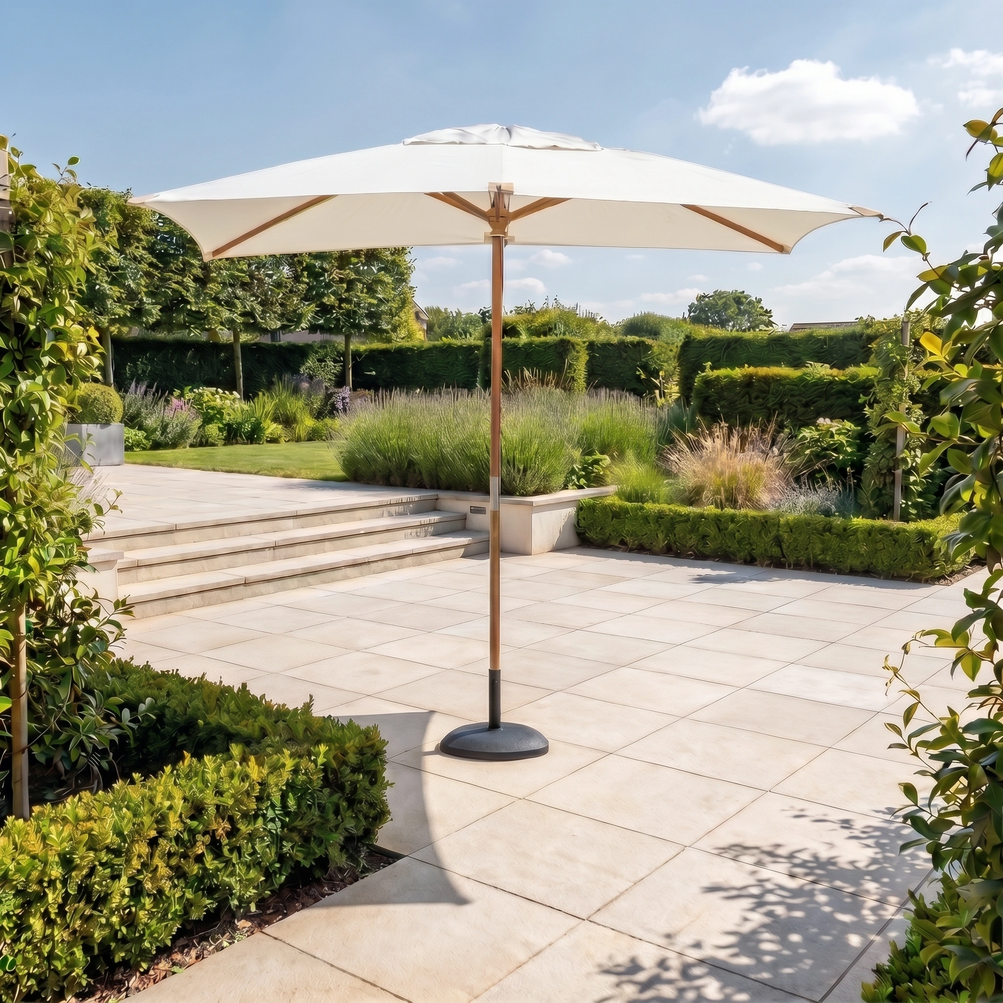 The Styx 3m x 2m Rectangular Deluxe Wooden Parasol in Beige stands on a tiled terrace in a lush green garden beneath a blue sky.