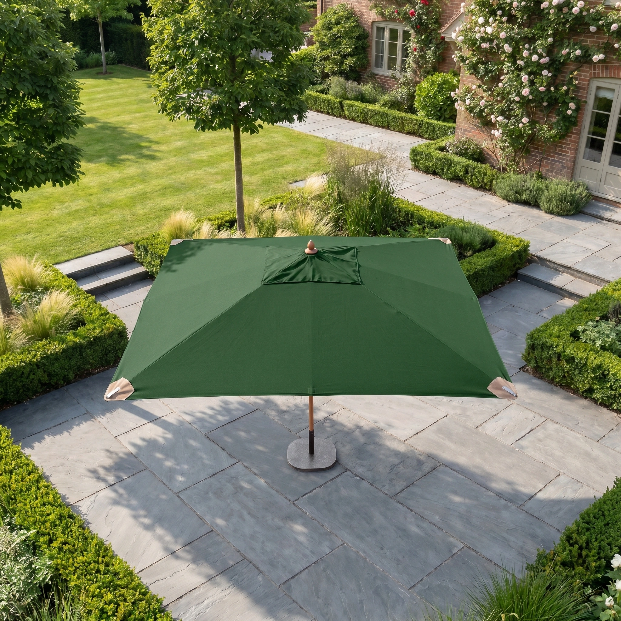 The Styx 3m x 2m Rectangular Deluxe Wooden Parasol in Green is open on a stone patio surrounded by manicured bushes.