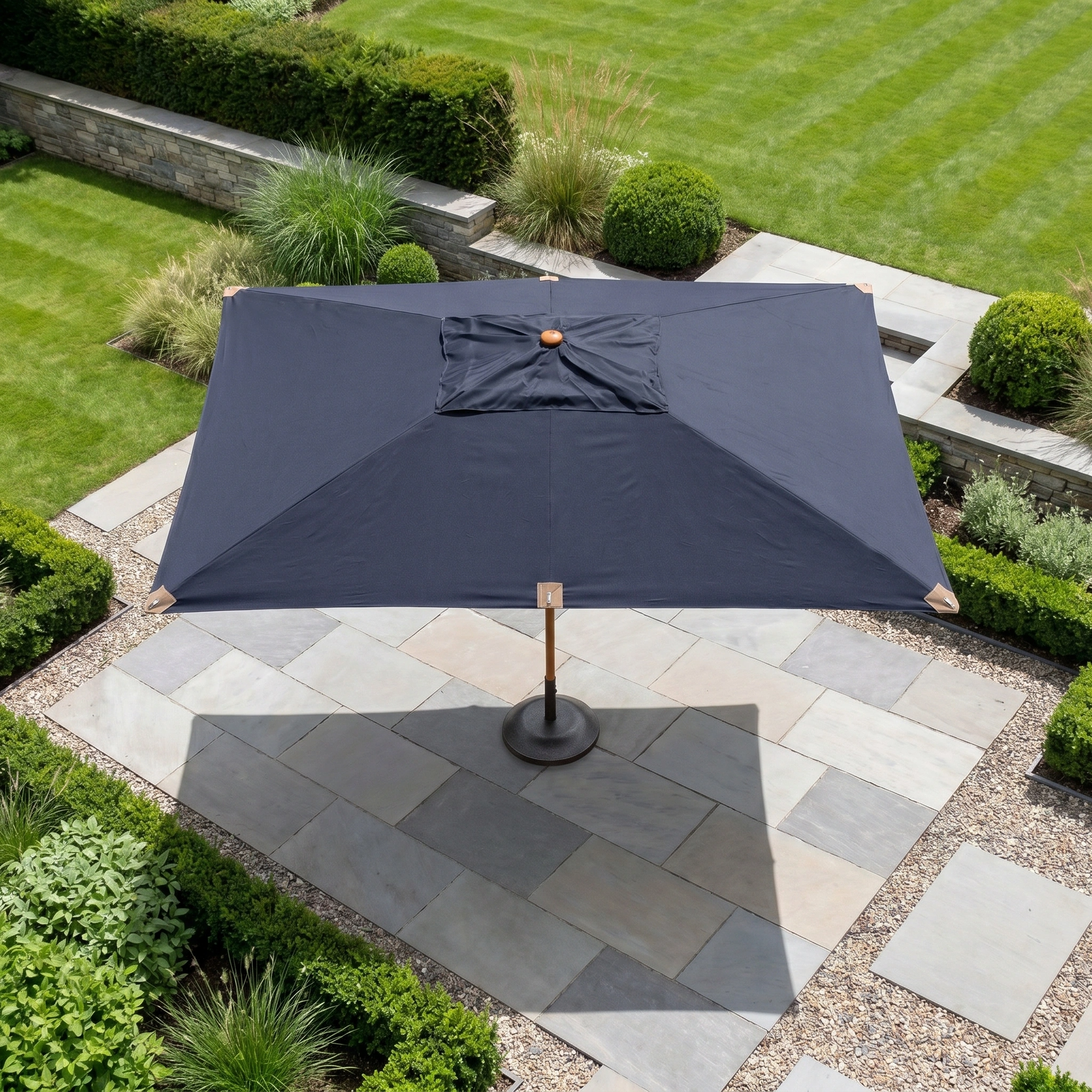 A Styx 3m x 2m Rectangular Deluxe Wooden Parasol in Navy shades a stone patio in a neatly landscaped garden.
