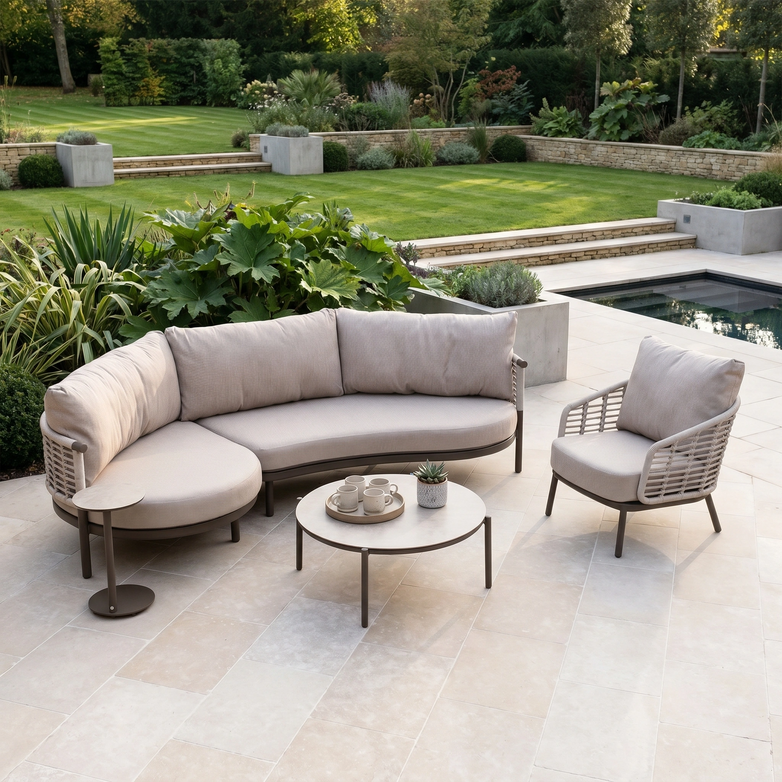 The Sutera Curved Chaise Sofa Set with Armchair in Putty features all-weather cushions, perfect for patios overlooking landscaped gardens and pools.