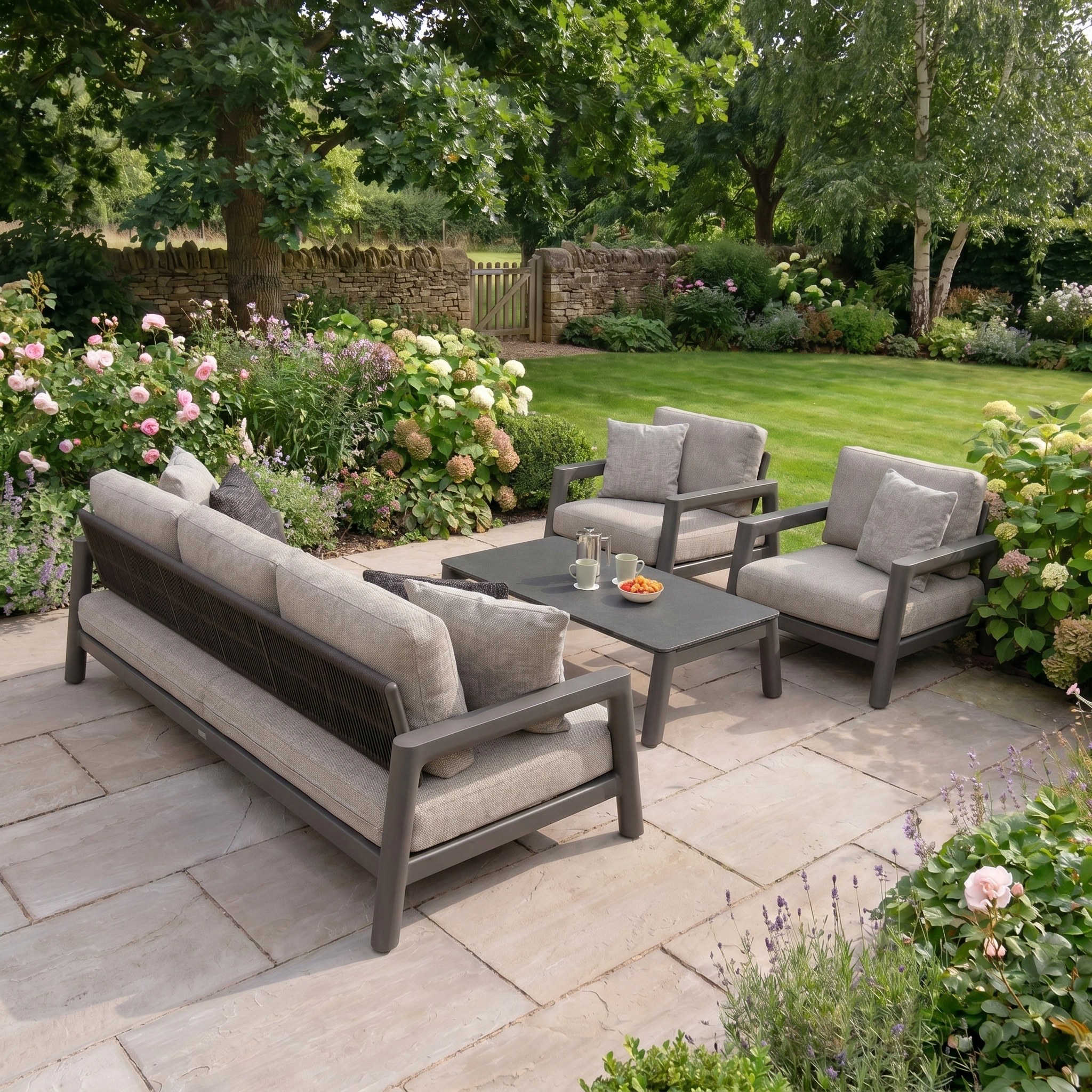 Theia 3 Seat Sofa Set in Truffle sits on a patio with a coffee table, surrounded by flowers and garden, creating a stylish outdoor furniture setup.