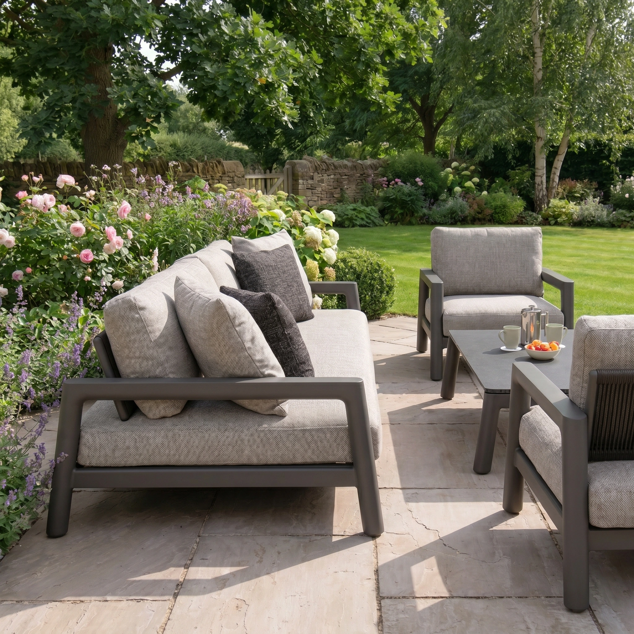 Modern patio featuring the Theia 3 Seat Sofa Set in Truffle with gray cushions, a sleek coffee table, and a lush garden backdrop—an inviting space for relaxing in style with contemporary outdoor furniture.