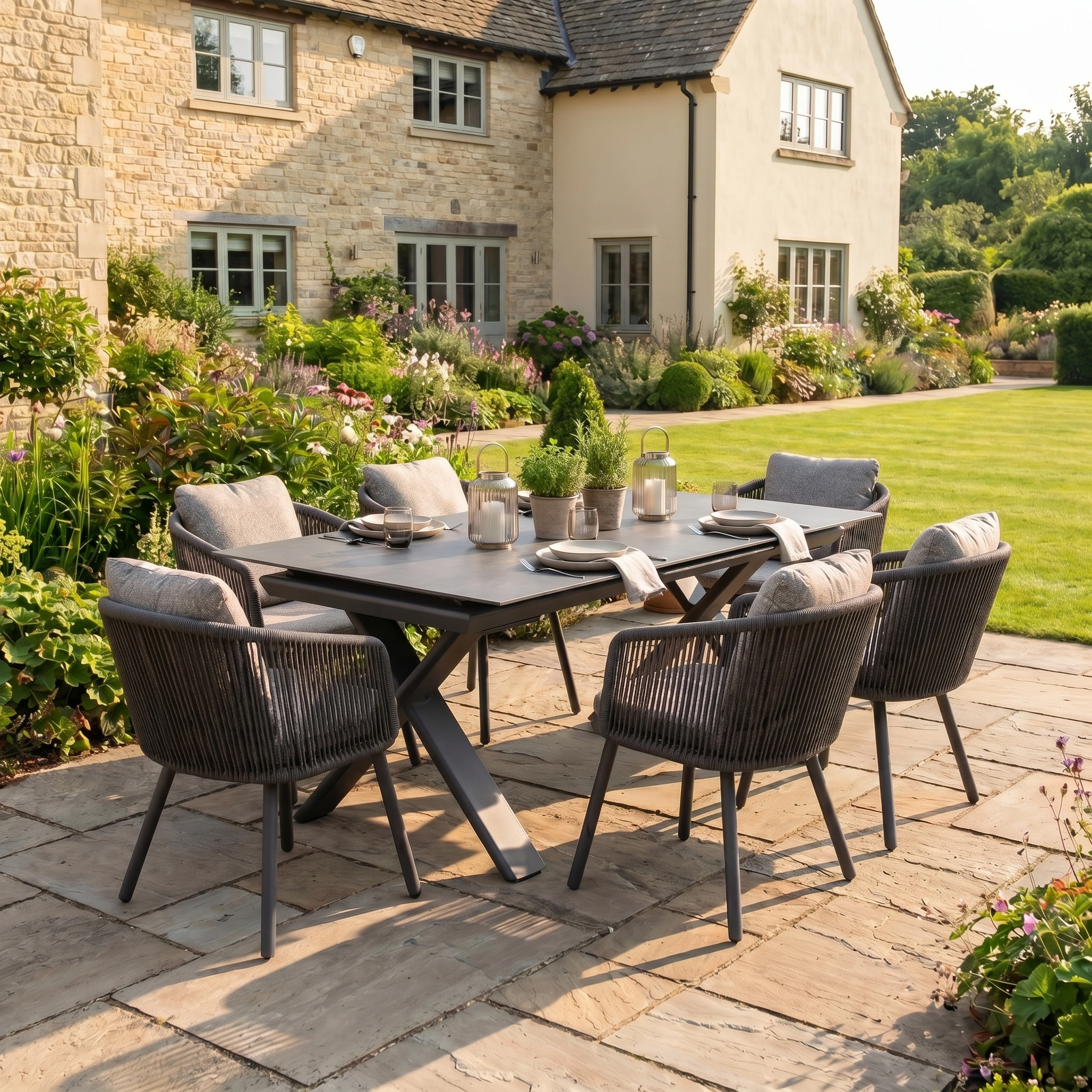Enhance your outdoor space with the Theia 6 Seat Rope Dining Set with Albatross Extending Table in Truffle, featuring six chairs—perfect for garden dining on a stone patio surrounded by greenery and a charming house backdrop.