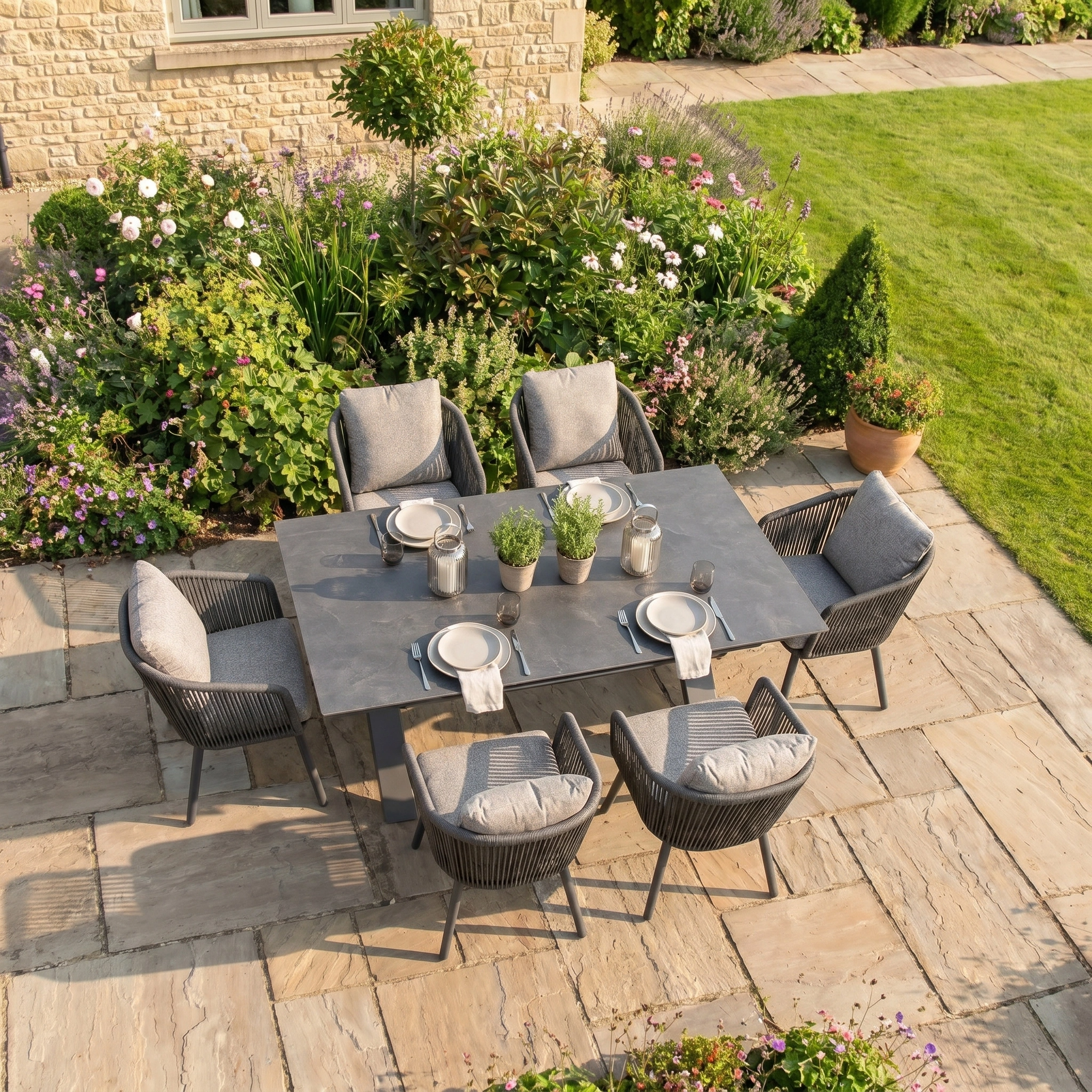 Theia 6 Seat Rope Dining Set with Albatross Extending Table in Truffle arranged for a meal on a beautiful lawn, surrounded by lush garden furniture.