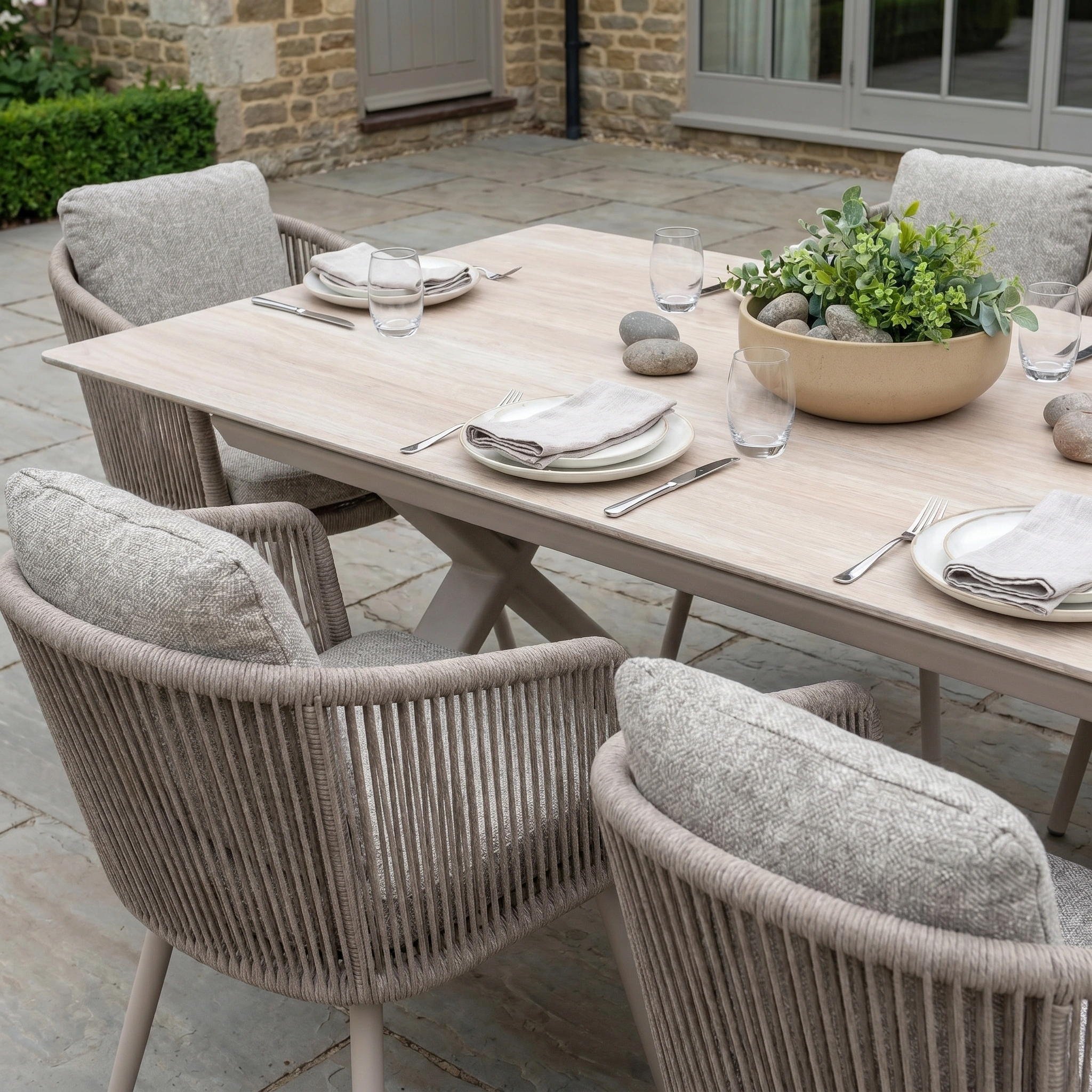 Theia 8 Seat Rope Dining Set with Albatross Extending Table in Oatmeal features four cushioned chairs, plates, glasses, and a centerpiece—ideal for alfresco meals or extending to accommodate extra guests.