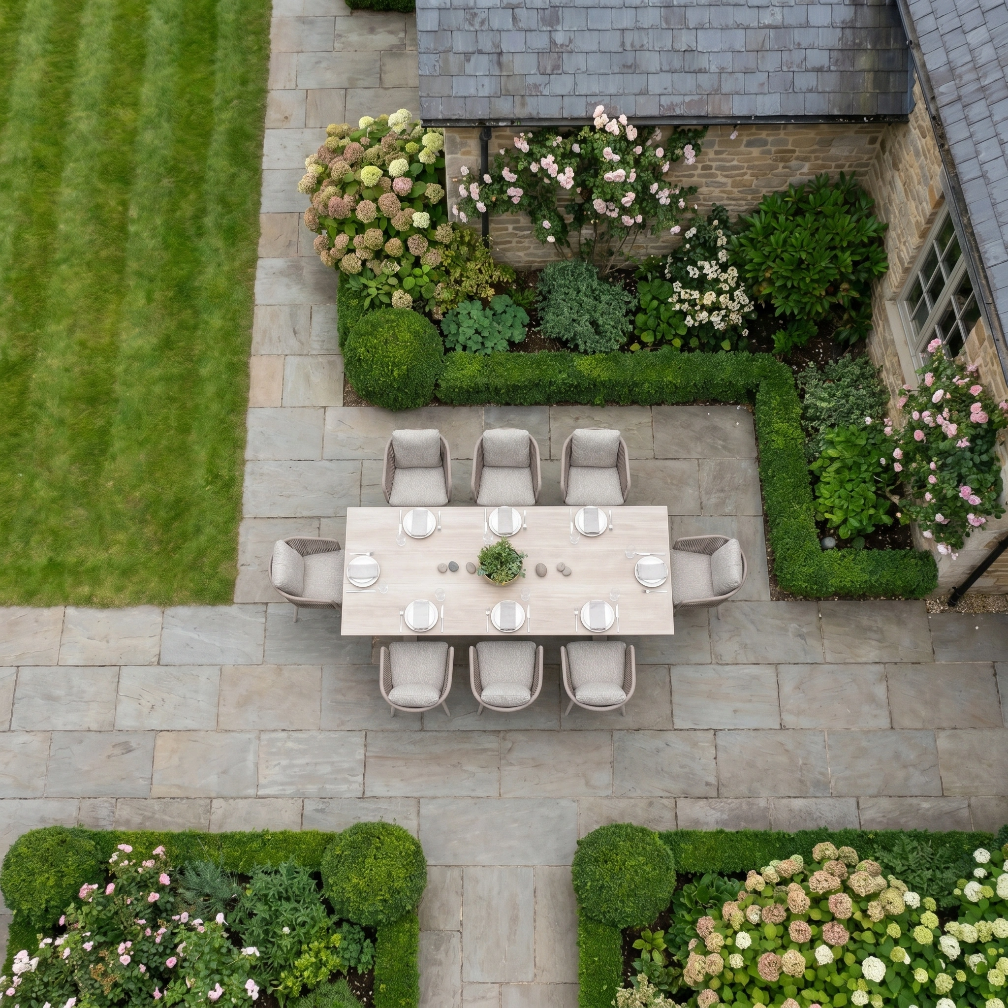 Aerial view of the Theia 8 Seat Rope Dining Set with Albatross Extending Table in Oatmeal on a stone patio, creating an elegant outdoor dining space amid lush gardens and hedges.
