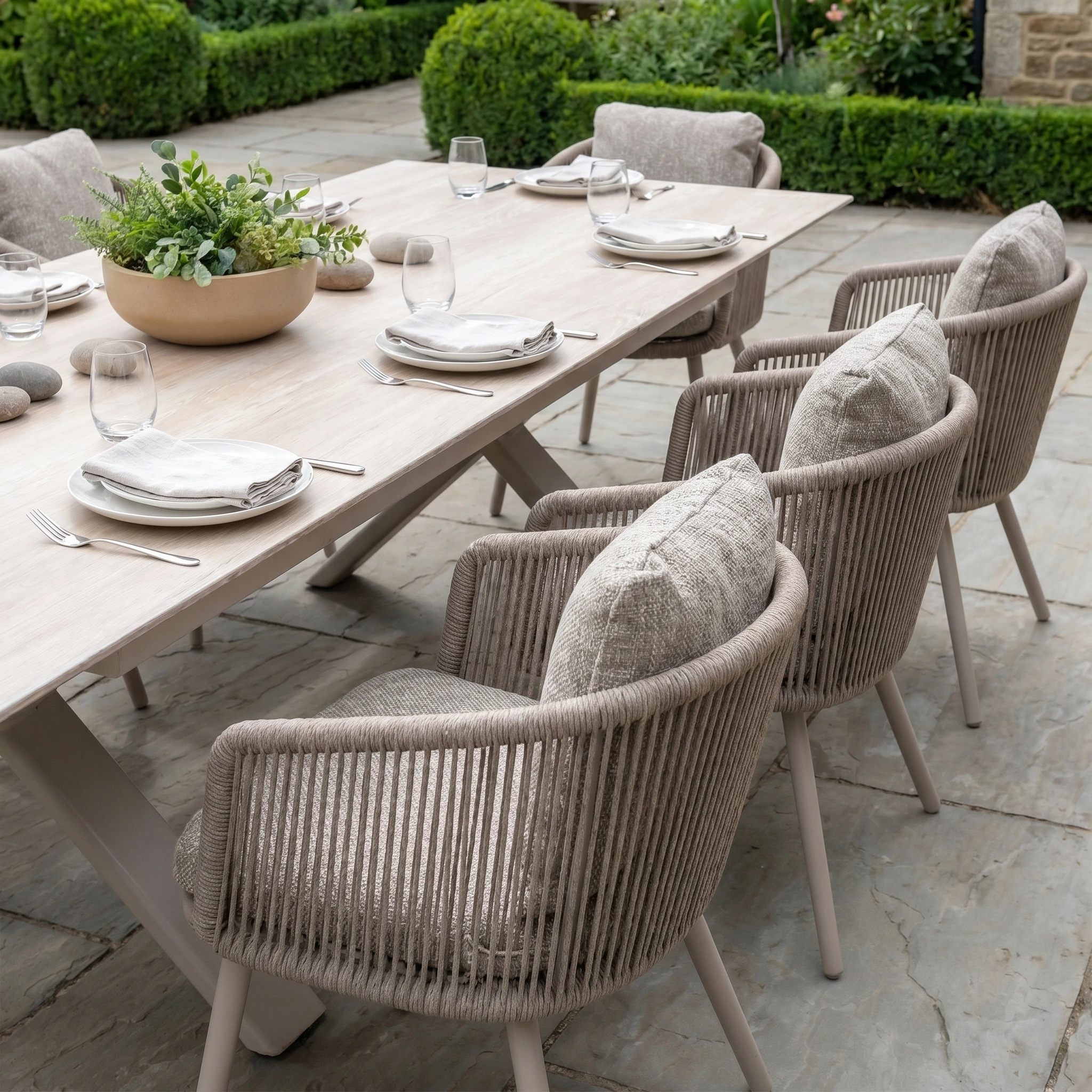 Theia 8 Seat Rope Dining Set with Albatross Extending Table in Oatmeal, complete with eight cushioned chairs and elegant tableware, arranged on a stone patio.