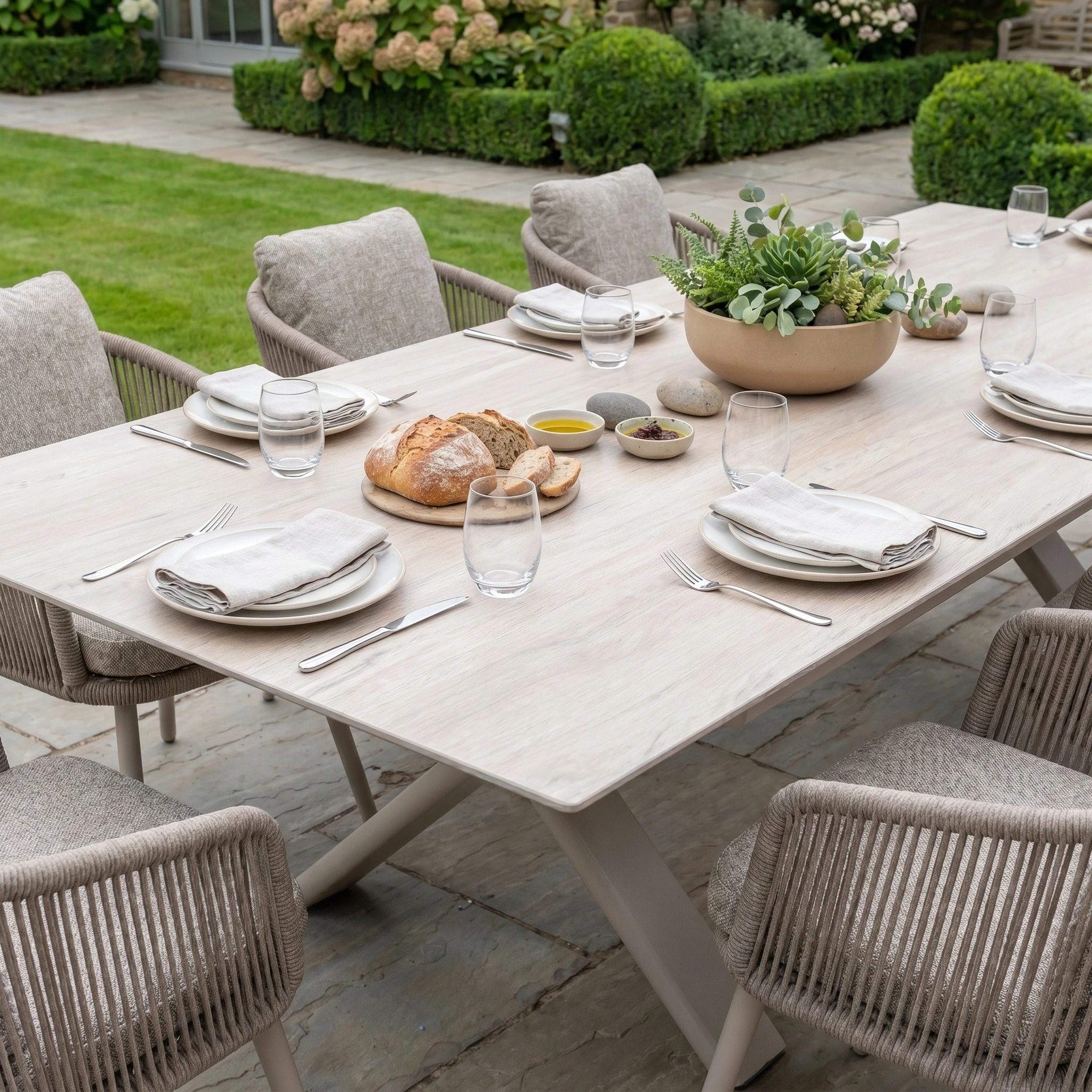 Host perfect gatherings with the Theia 8 Seat Rope Dining Set, featuring an Albatross Extending Table in Oatmeal, set with plates, glasses, napkins, bread, dips, and a succulent centerpiece.