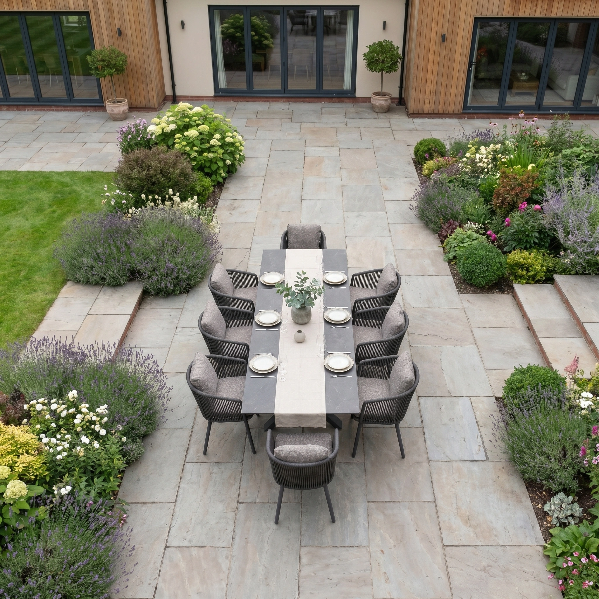 The Theia 8 Seat Rope Dining Set with Albatross Extending Table in Truffle offers stylish alfresco dining for eight—ideal outdoor garden furniture for your stone patio, surrounded by lush greenery and blooms.