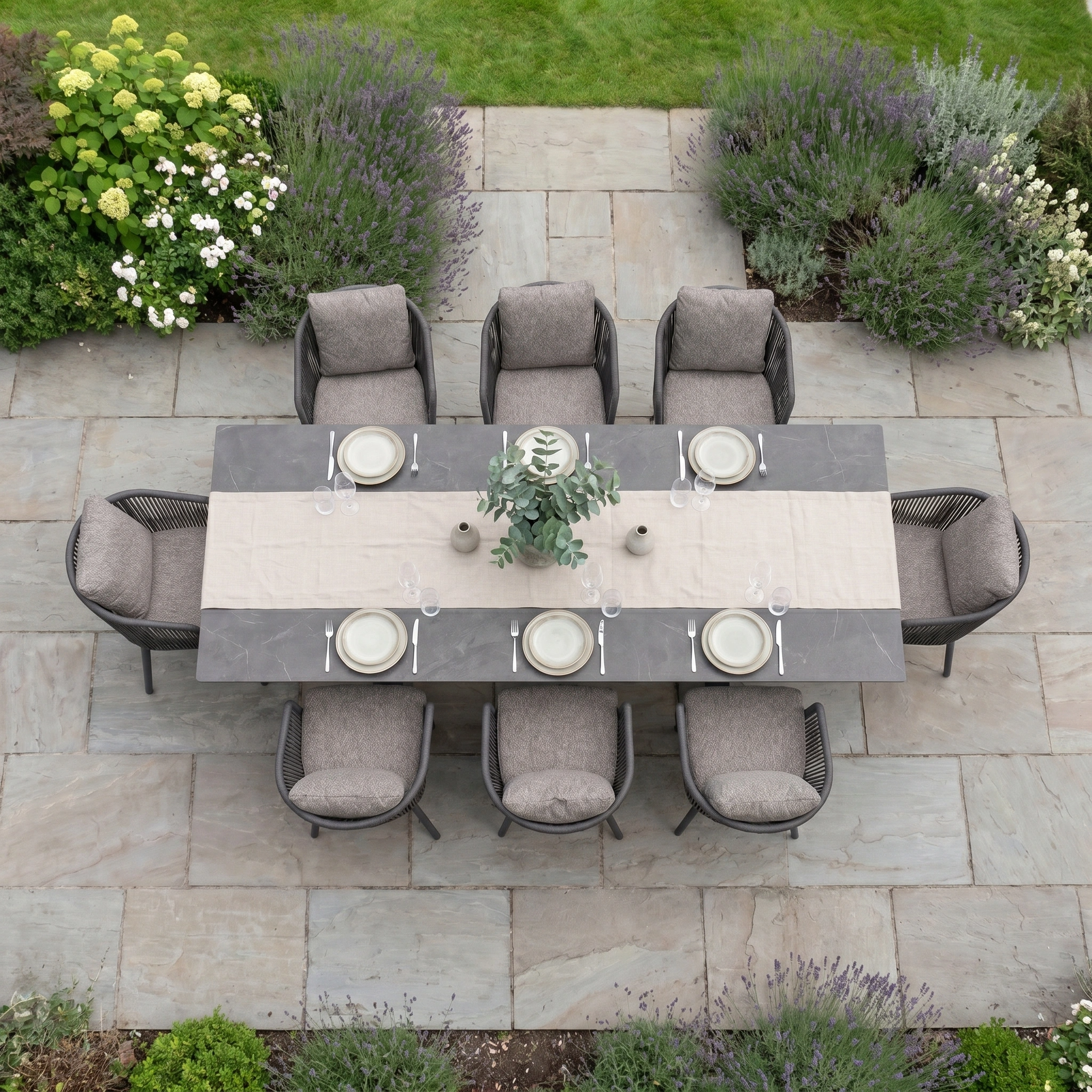 Theia 8 Seat Rope Dining Set with Albatross Extending Table in Truffle, featuring neutral chairs, a runner, plates, and greenery, is arranged stylishly on a stone patio for elegant outdoor dining.