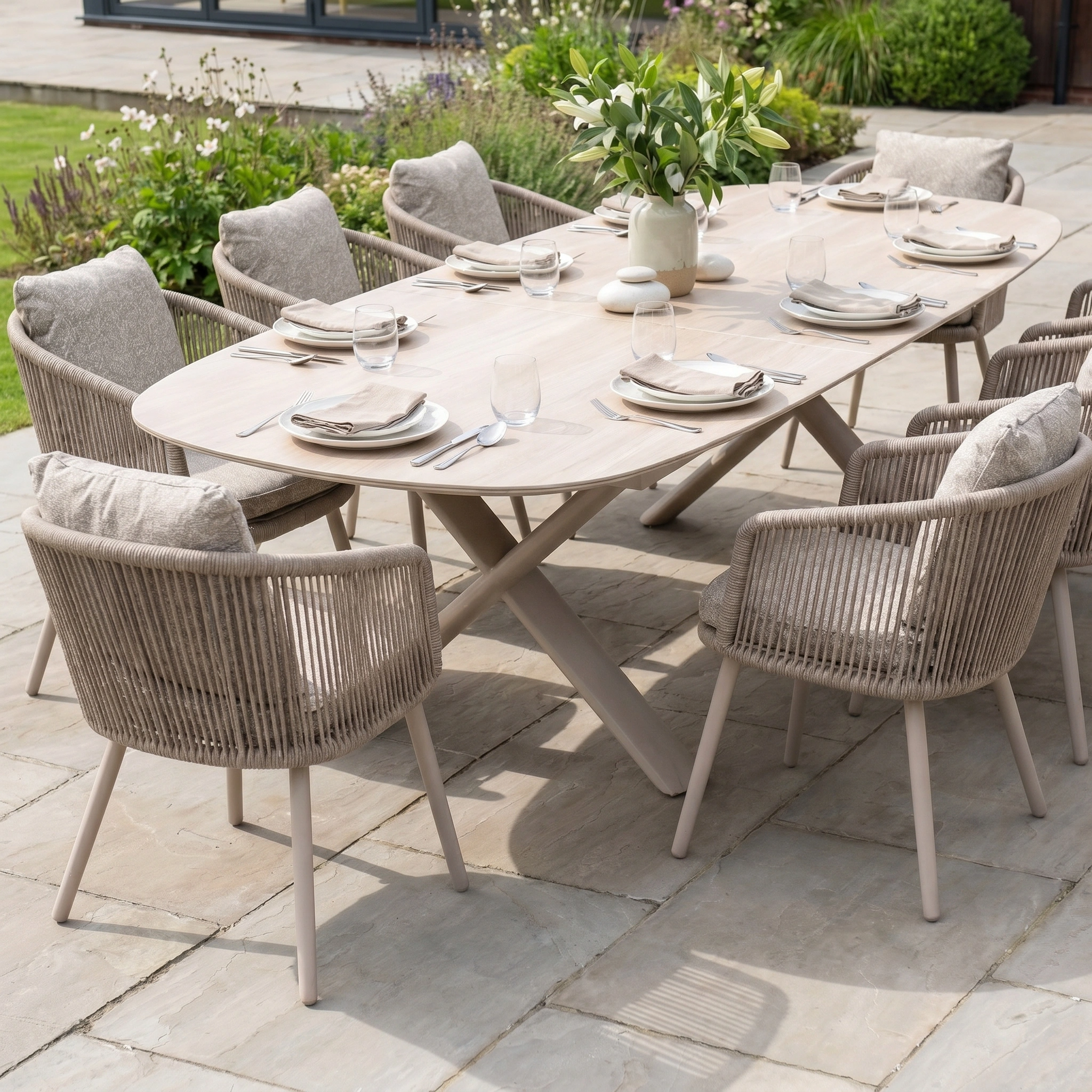Theia 8 Seat Oval Rope Dining Set with Albatross Extending Table in Oatmeal features rope dining chairs, neutral-toned plates and glasses, and a floral vase atop an elegant extending garden table.