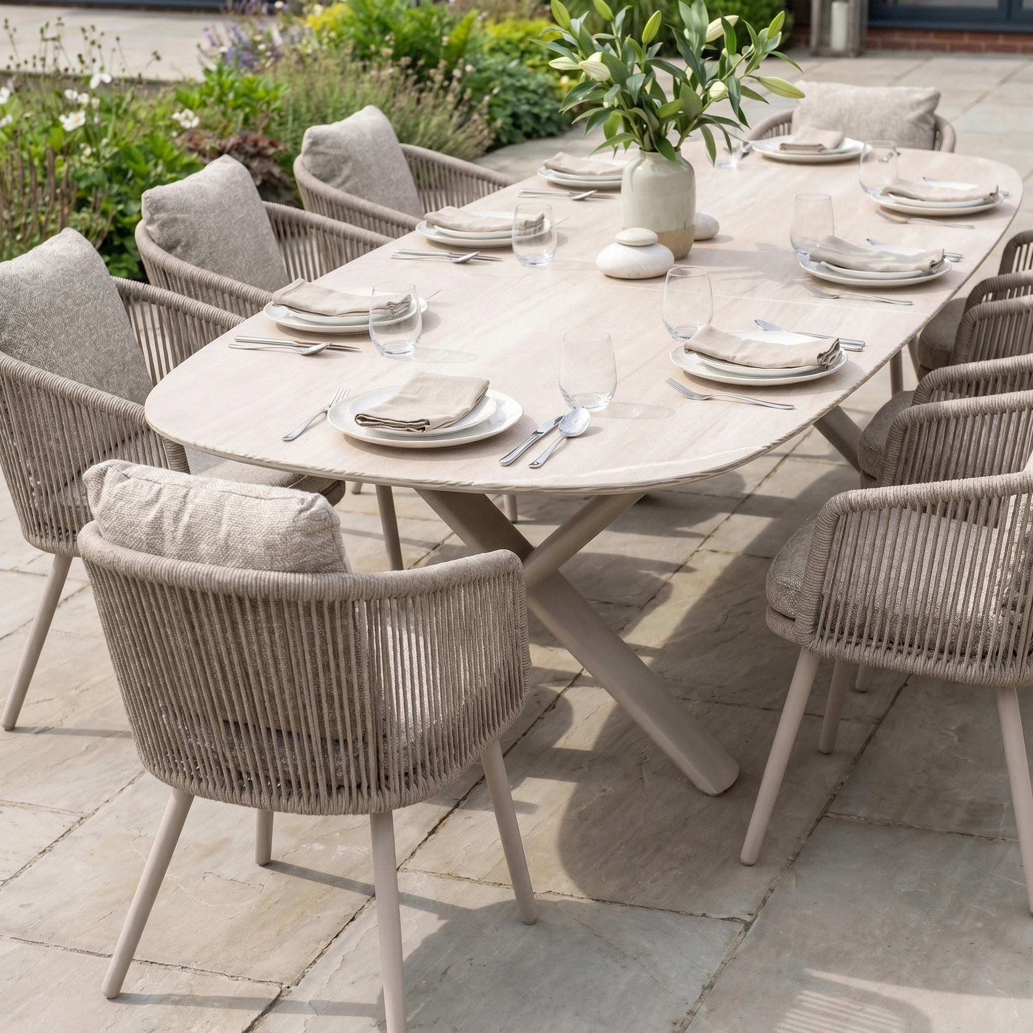 The Theia 8 Seat Oval Rope Dining Set with Albatross Extending Table in Oatmeal features cushioned rope dining chairs and seating for eight, complete with neutral plates, glasses, and cutlery for outdoor dining.