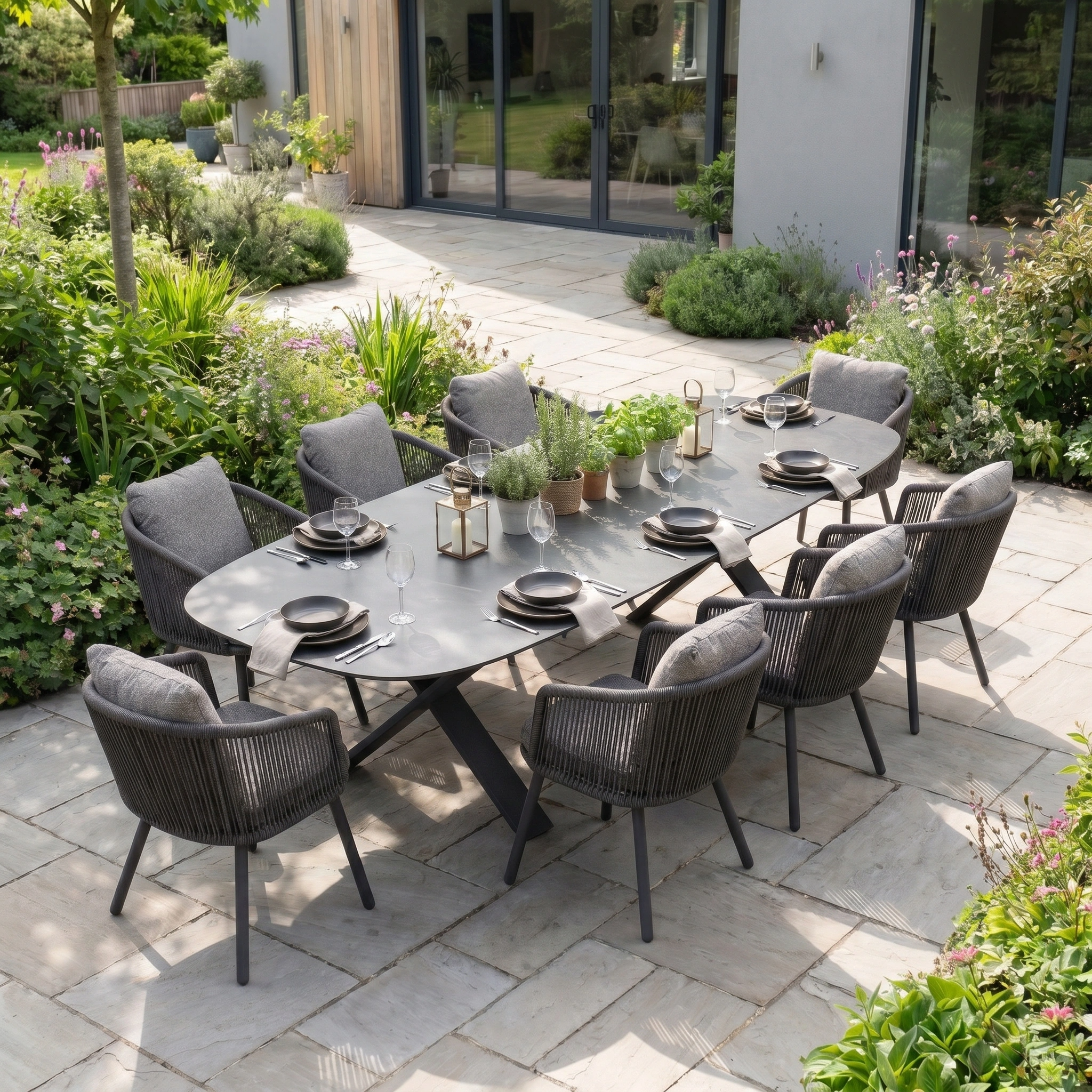 Theia 8 Seat Oval Rope Dining Set with Albatross Extending Table in Truffle, arranged for outdoor dining on a garden patio amid lush greenery.