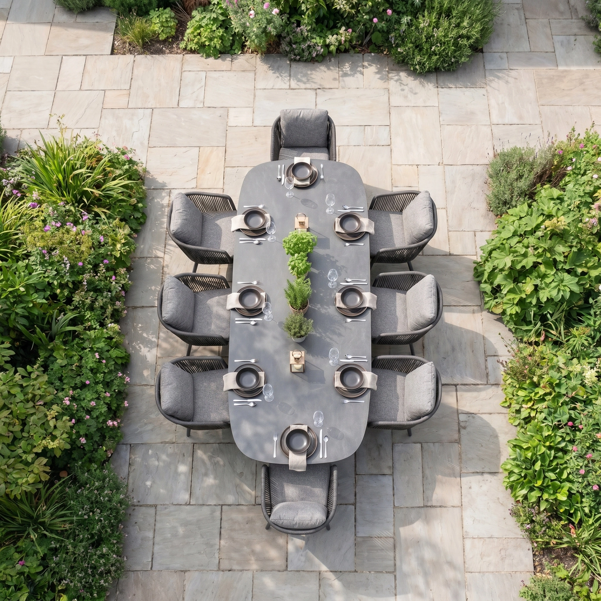 Theia 8 Seat Oval Rope Dining Set with Albatross Extending Table in Truffle, seating eight, is arranged outdoors amidst greenery and stone paving, captured from an overhead view.