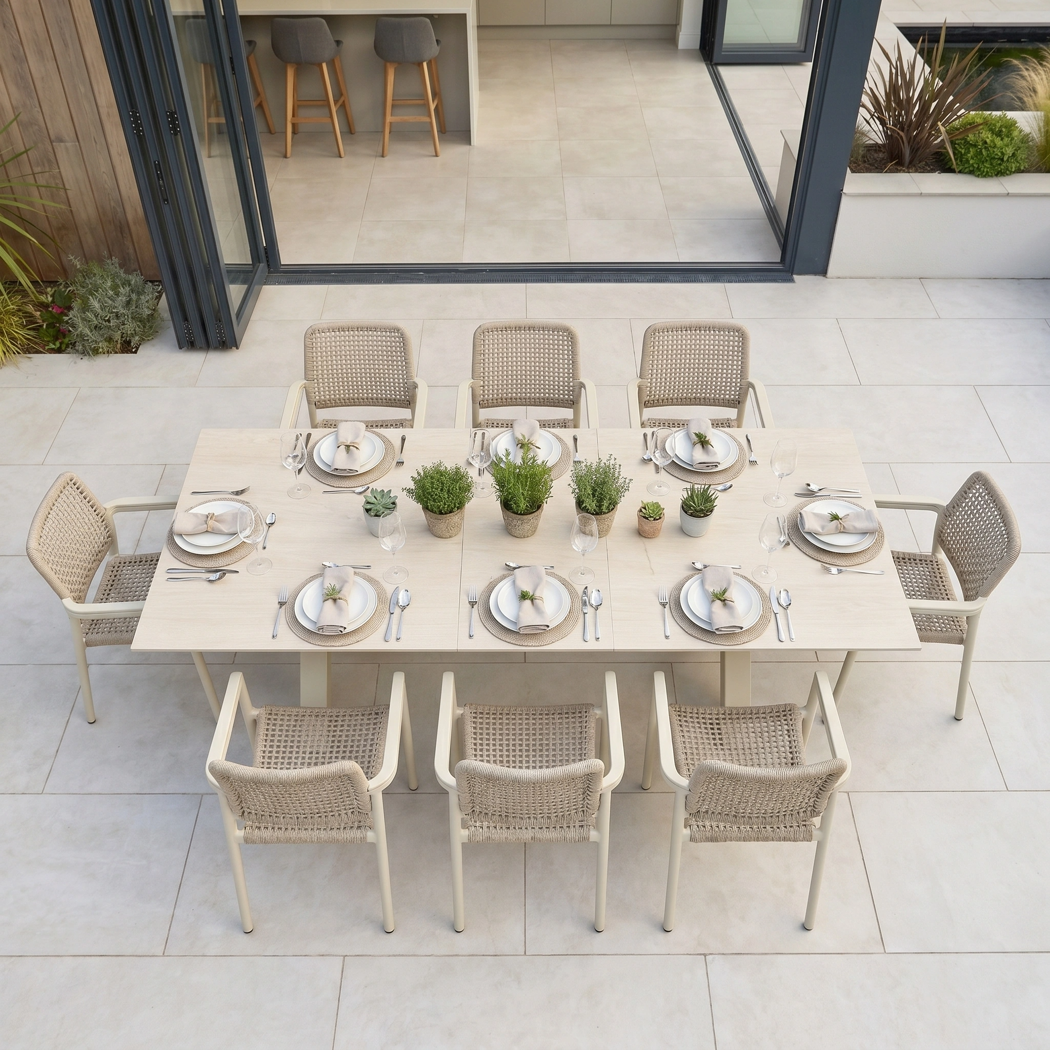 The Tolo 8 Seat Extending Dining Set in Oatmeal features a spacious sintered stone table, perfect for outdoor dining with plates and glasses, beautifully arranged on a patio near an open kitchen.