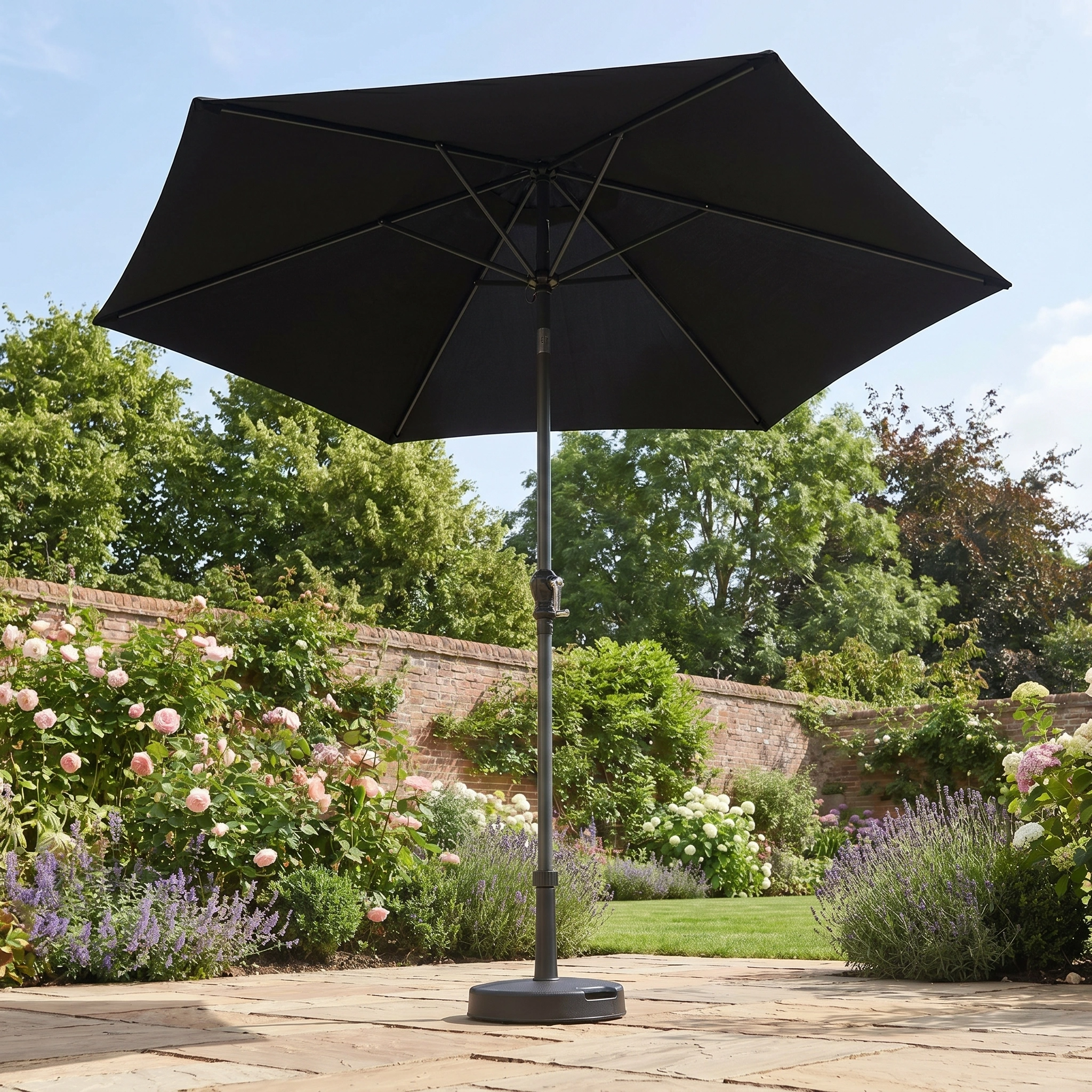 The Triton 2.5m Round Aluminium Parasol in Black stands open on a stone patio in a lush garden, offering stylish UV protection.