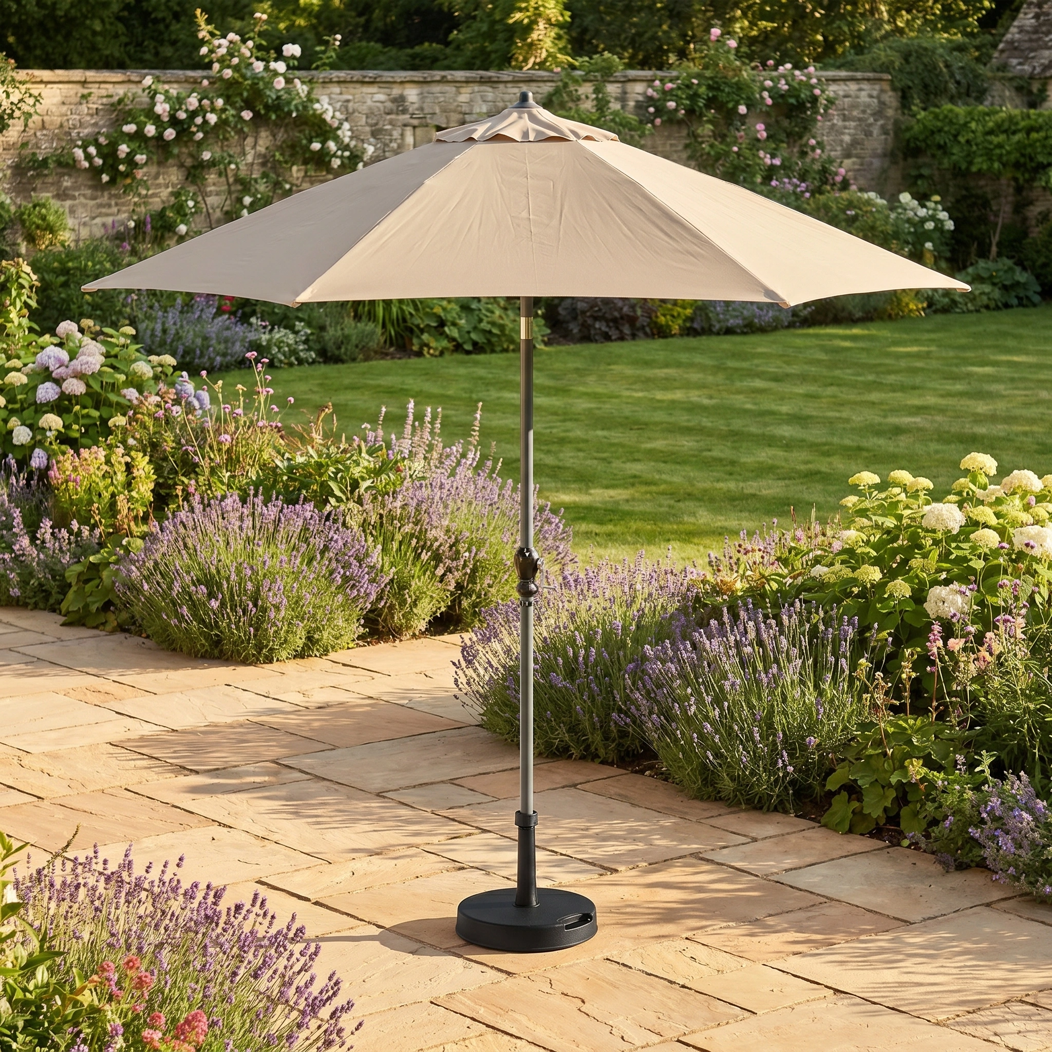 A Triton 2.5m Round Aluminium Parasol in Khaki stands open on a stone patio, surrounded by lavender and blooming bushes.