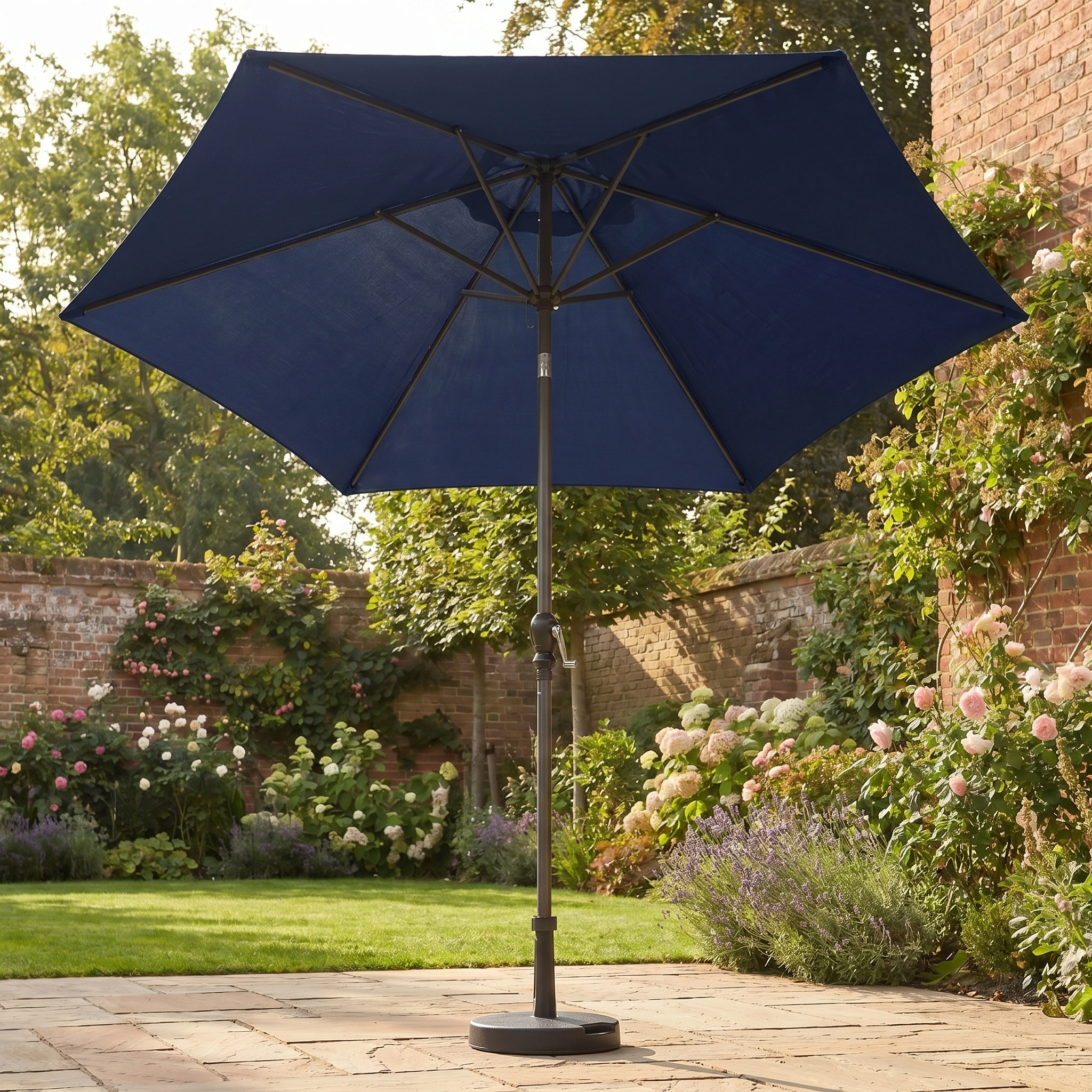 The Triton 2.5m Round Aluminium Parasol in Navy stands open on a stone patio, providing UV protection with a garden view in the background.
