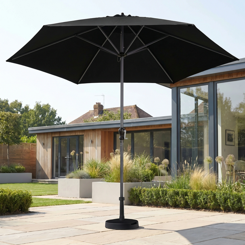 The Triton 3m Round Aluminium Parasol in Black stands open on a stone terrace in a modern garden, providing stylish UV protection.