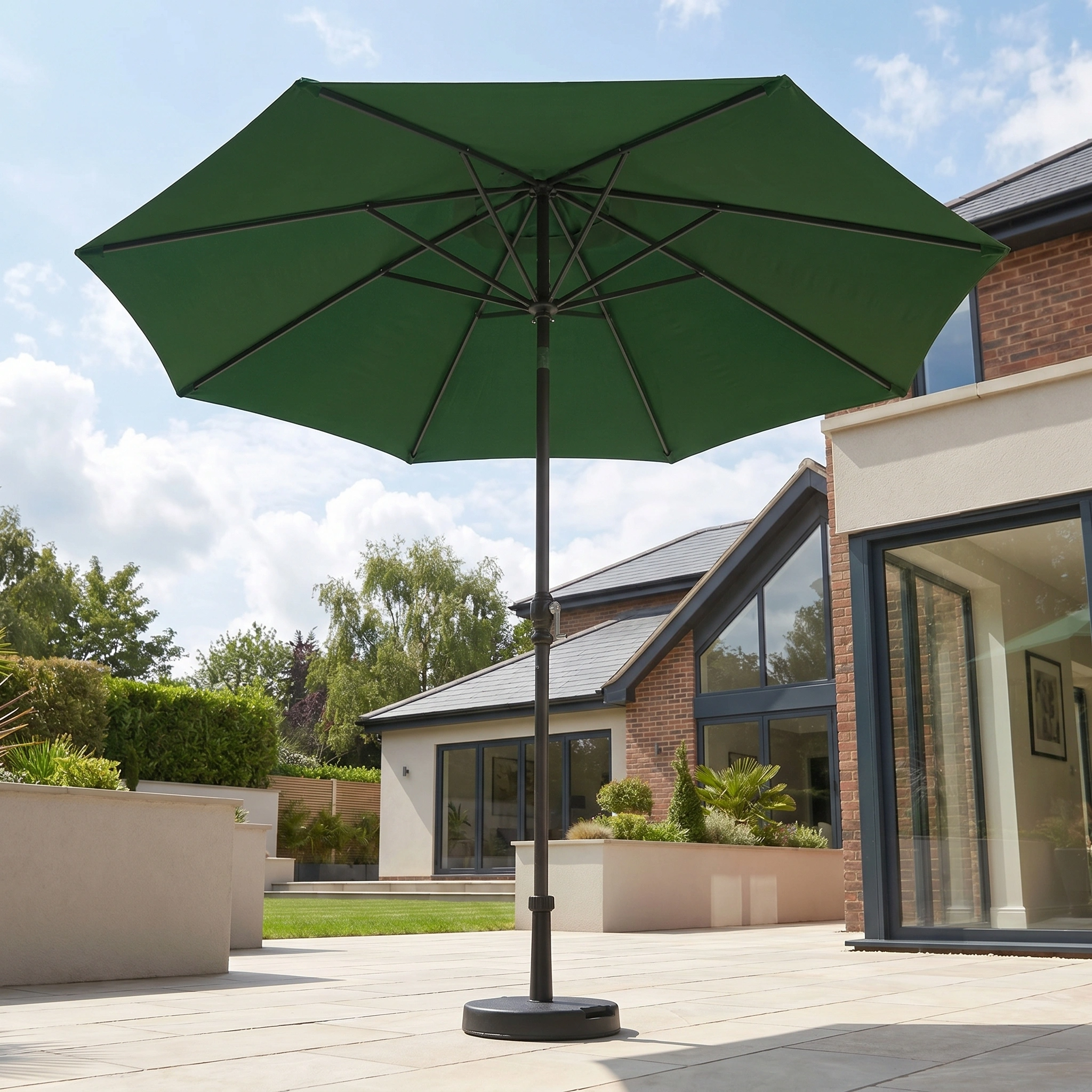 The Triton 3m Round Aluminium Parasol in Green stands open on a sunlit modern terrace, adding style and effective UV protection.