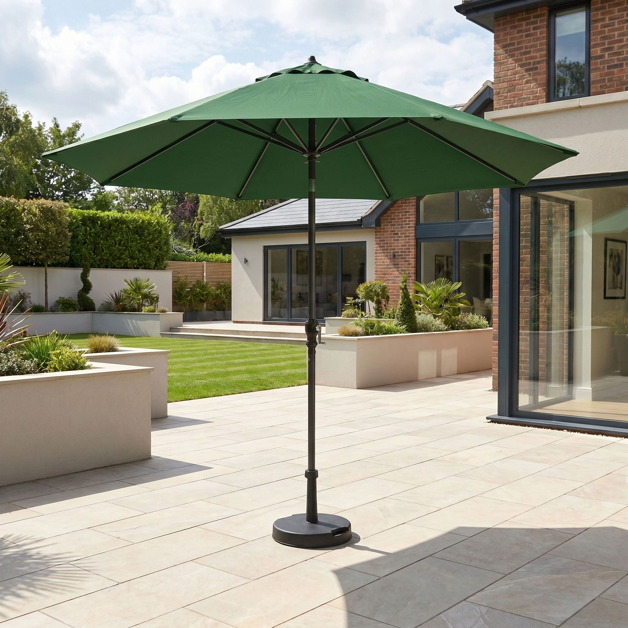 The Triton 3m Round Aluminium Parasol in Green stands on a light patio before a modern home with large windows, offering shade and style.