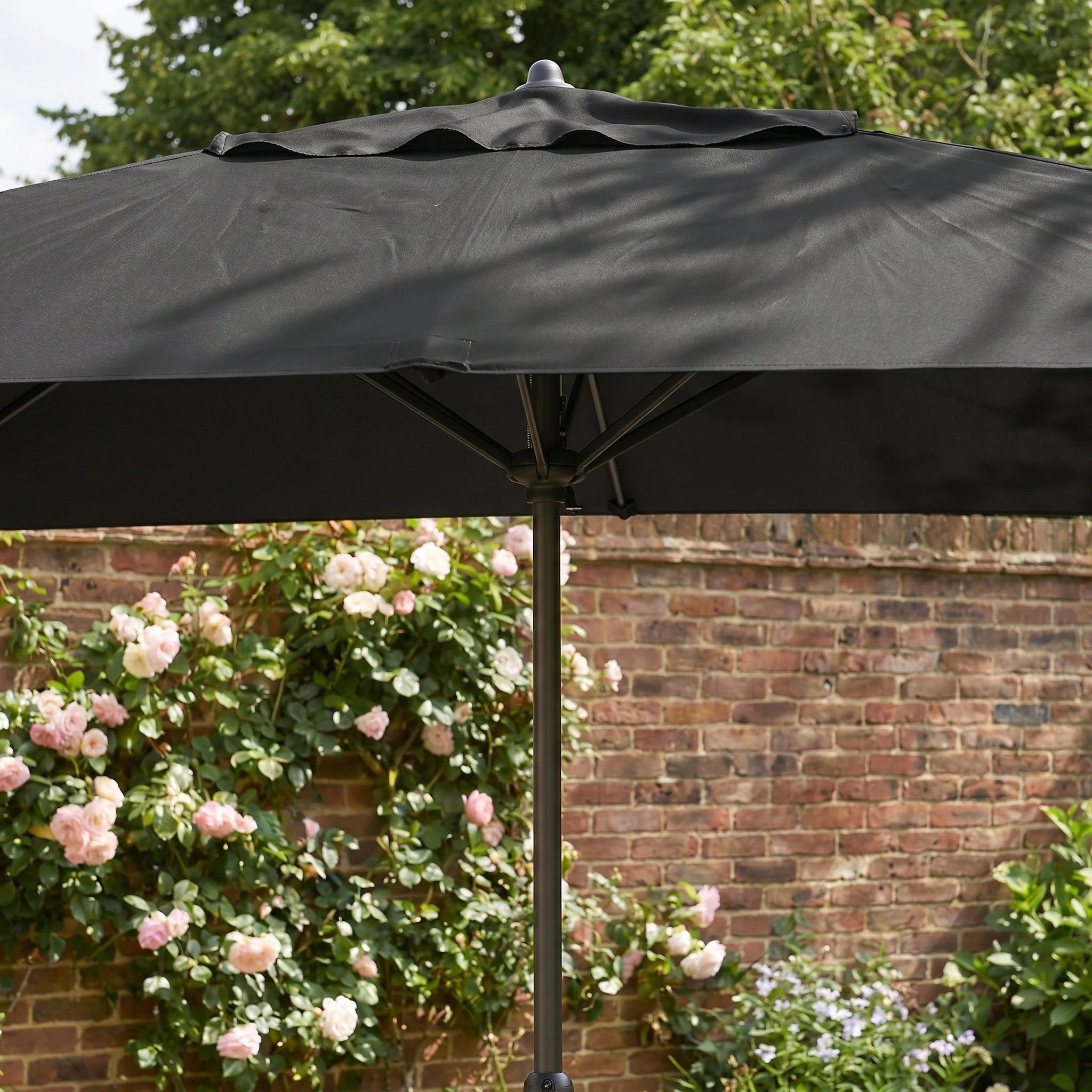 The Triton 3m x 2m Rectangular Aluminium Parasol in Black provides UV protection and stylish shade, making it perfect for gardens with blooming pink roses and a brick wall backdrop.