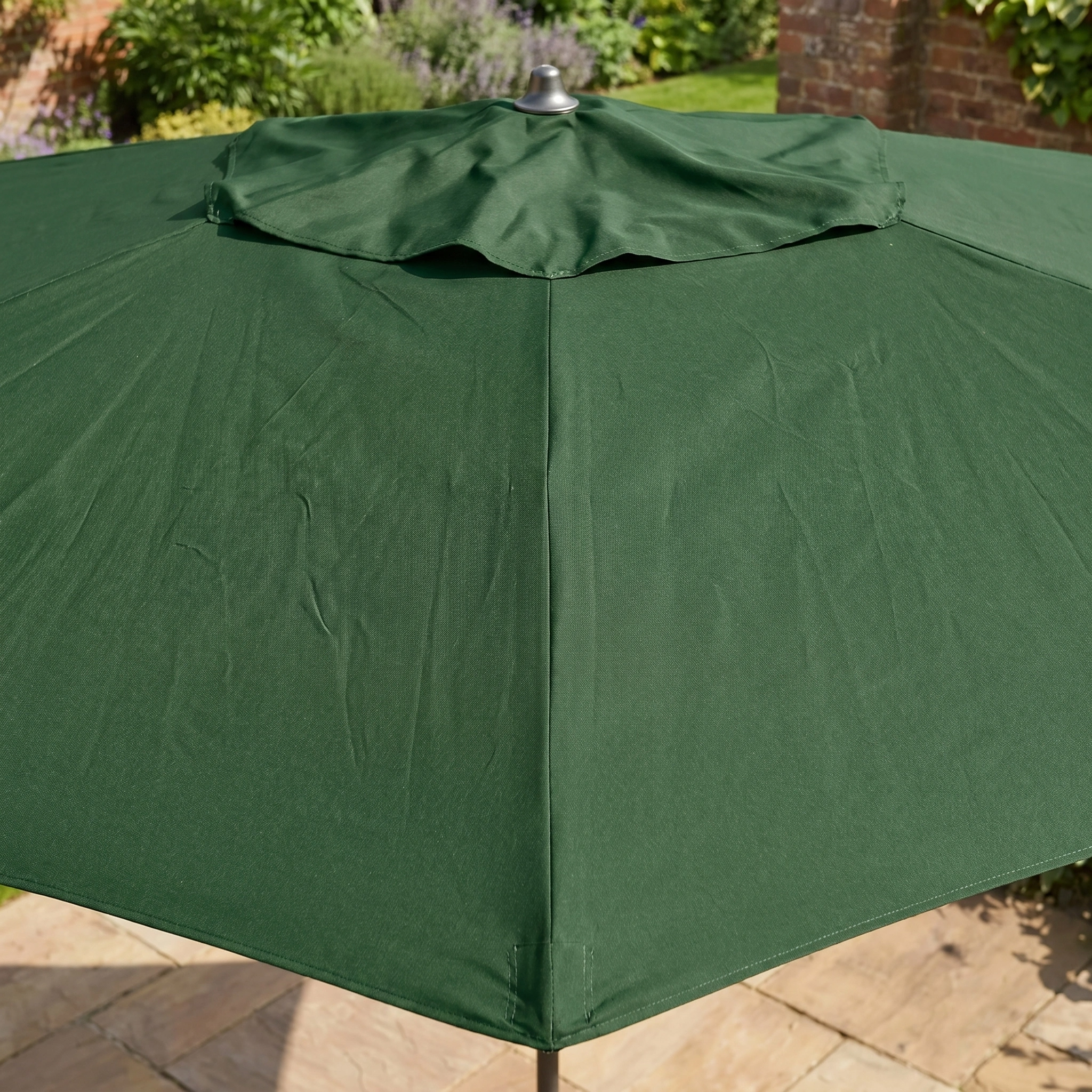 The Triton 3m x 2m Rectangular Aluminium Parasol in Green stands open on a stone patio, offering shade beside the garden and brick wall. Its sturdy aluminium frame combines style and durability in your outdoor space.