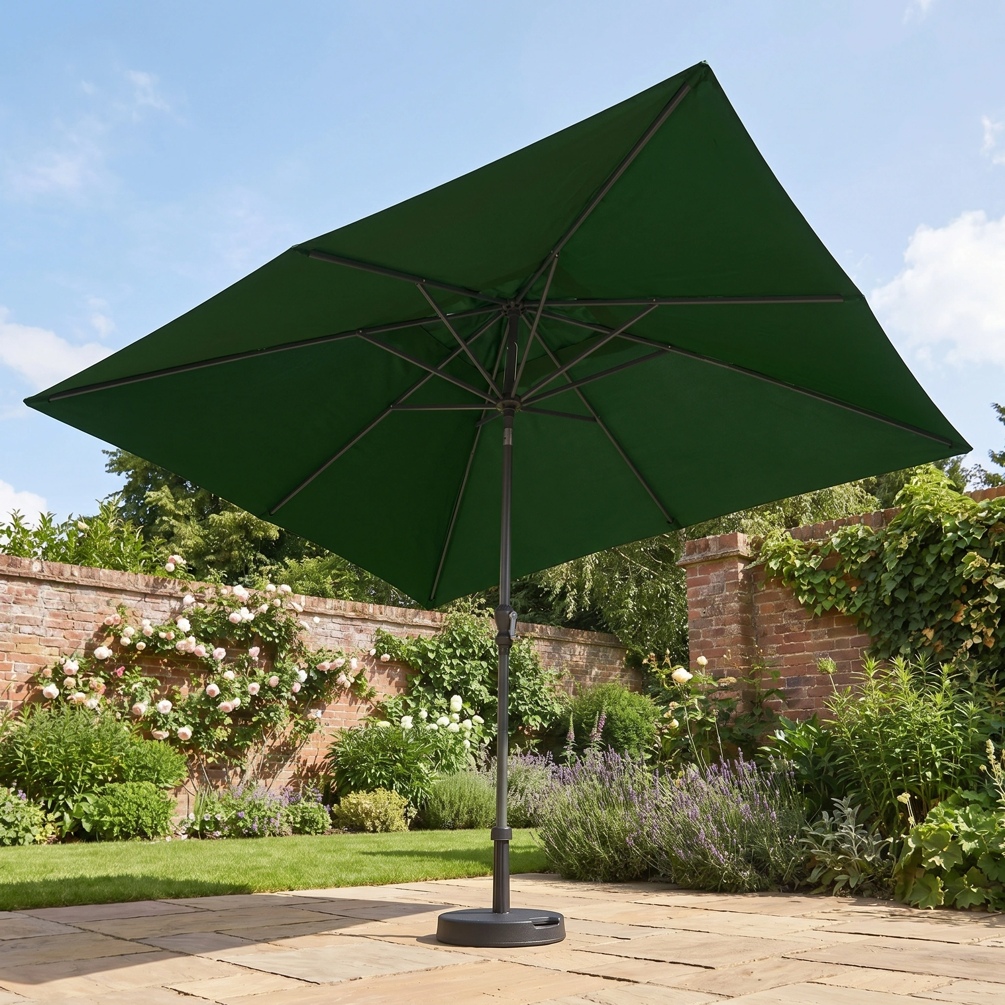 The Triton 3m x 2m Rectangular Aluminium Parasol in Green stands on a stone patio, surrounded by flowers and brick walls in a vibrant garden.