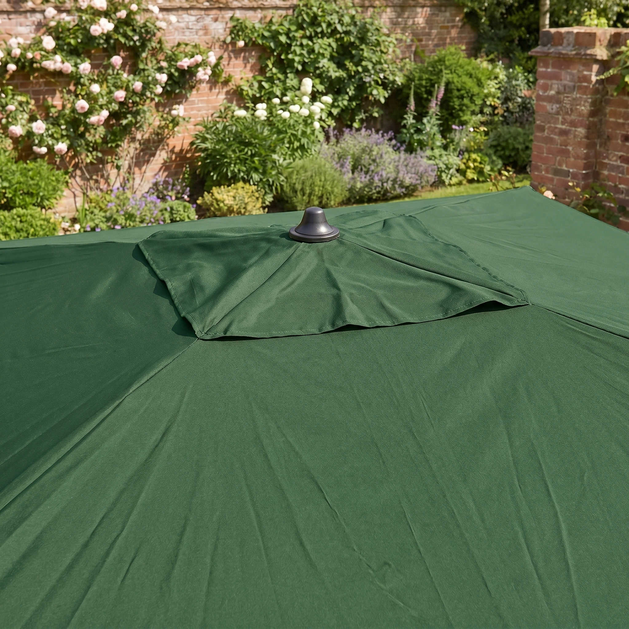 The Triton 3m x 2m Rectangular Aluminium Parasol in Green features a vented top and is ideal for adding shade and style to your garden or patio. Set against brick walls and blooming plants, it enhances any outdoor space.