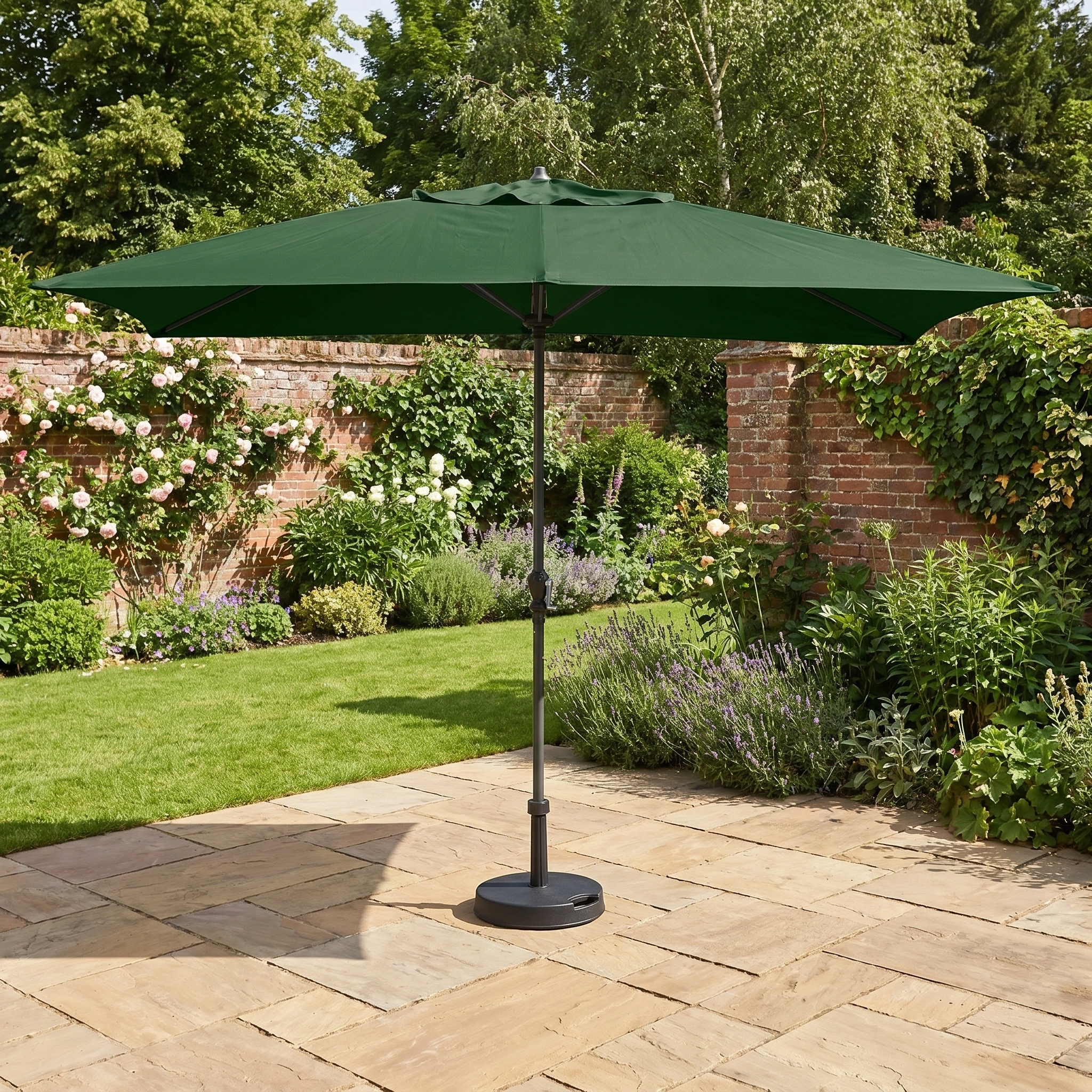 The Triton 3m x 2m Rectangular Aluminium Parasol in Green stands on a stone patio in a lush, flower-filled backyard, offering ample shade and comfort.