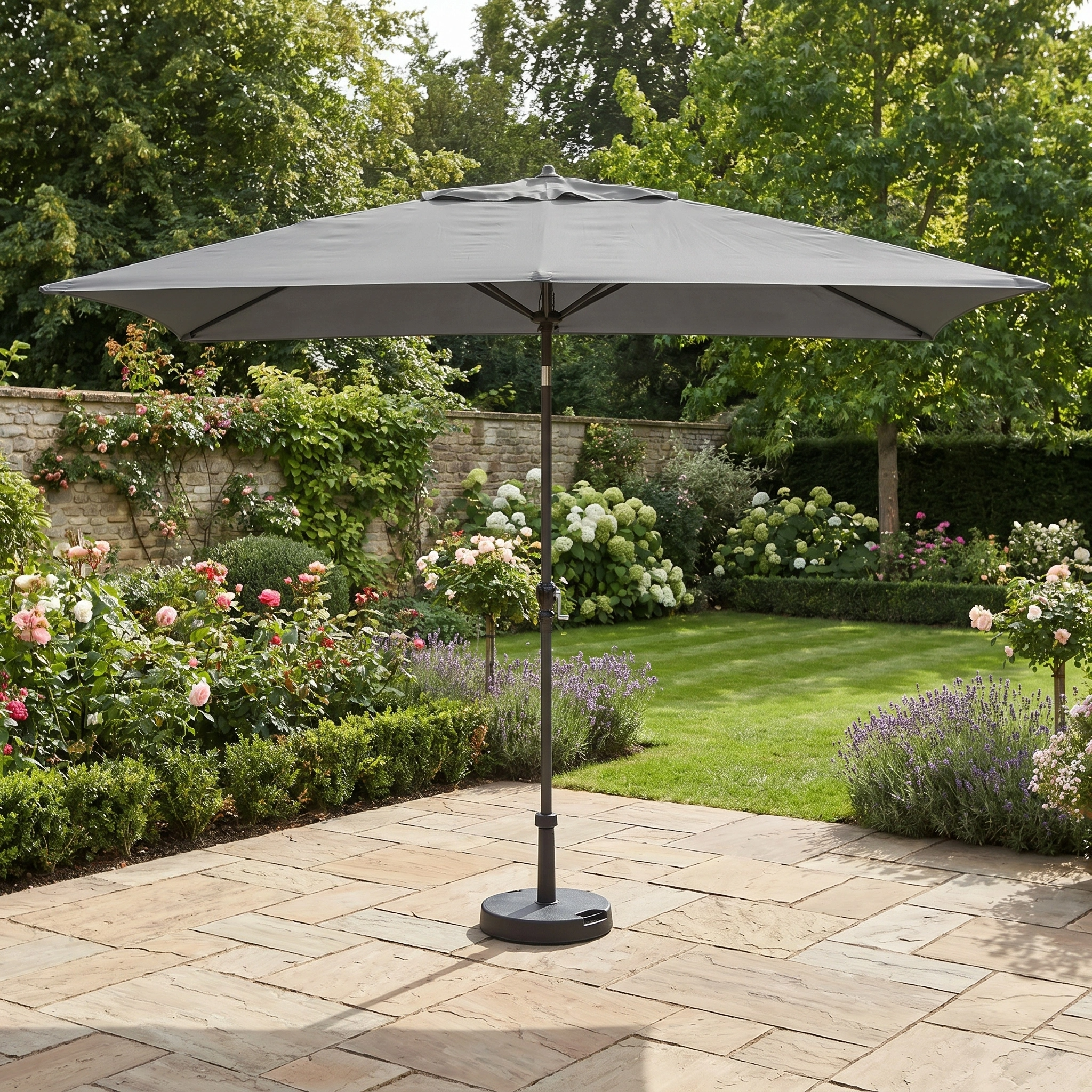 The Triton 3m x 2m Rectangular Aluminium Parasol in Grey stands on a stone terrace in a vibrant garden, providing reliable UV sun protection.