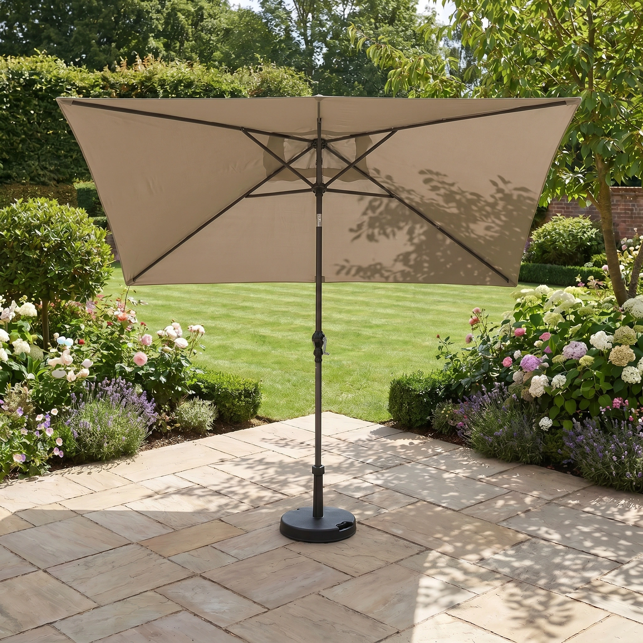 The Triton 3m x 2m Rectangular Aluminium Parasol in Khaki, designed to resist fading, stands on a stone patio amid garden flowers and a green lawn.