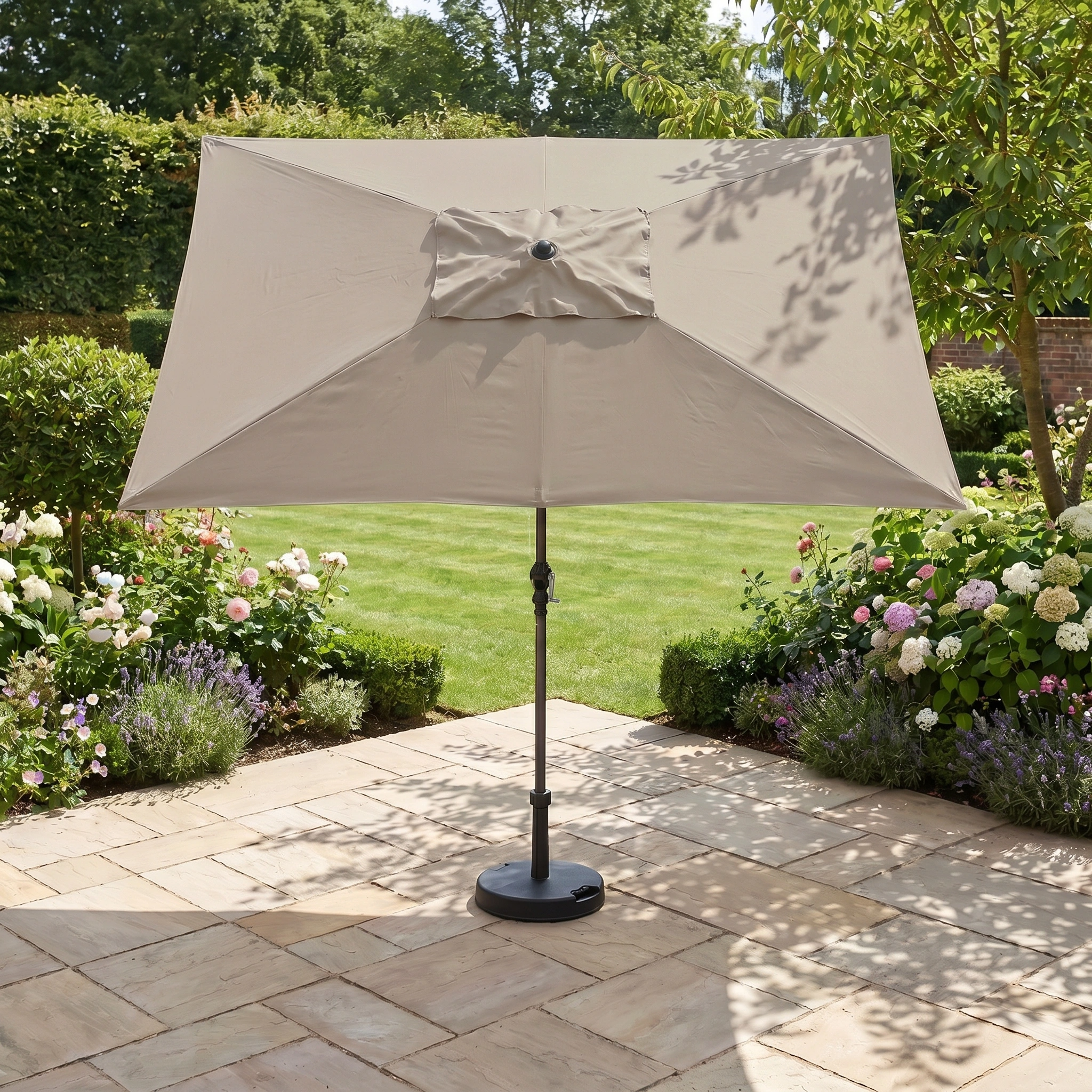The Triton 3m x 2m Rectangular Aluminium Parasol in Khaki provides fade-resistant, stylish shade on a stone terrace, surrounded by blooming garden flowers and greenery.