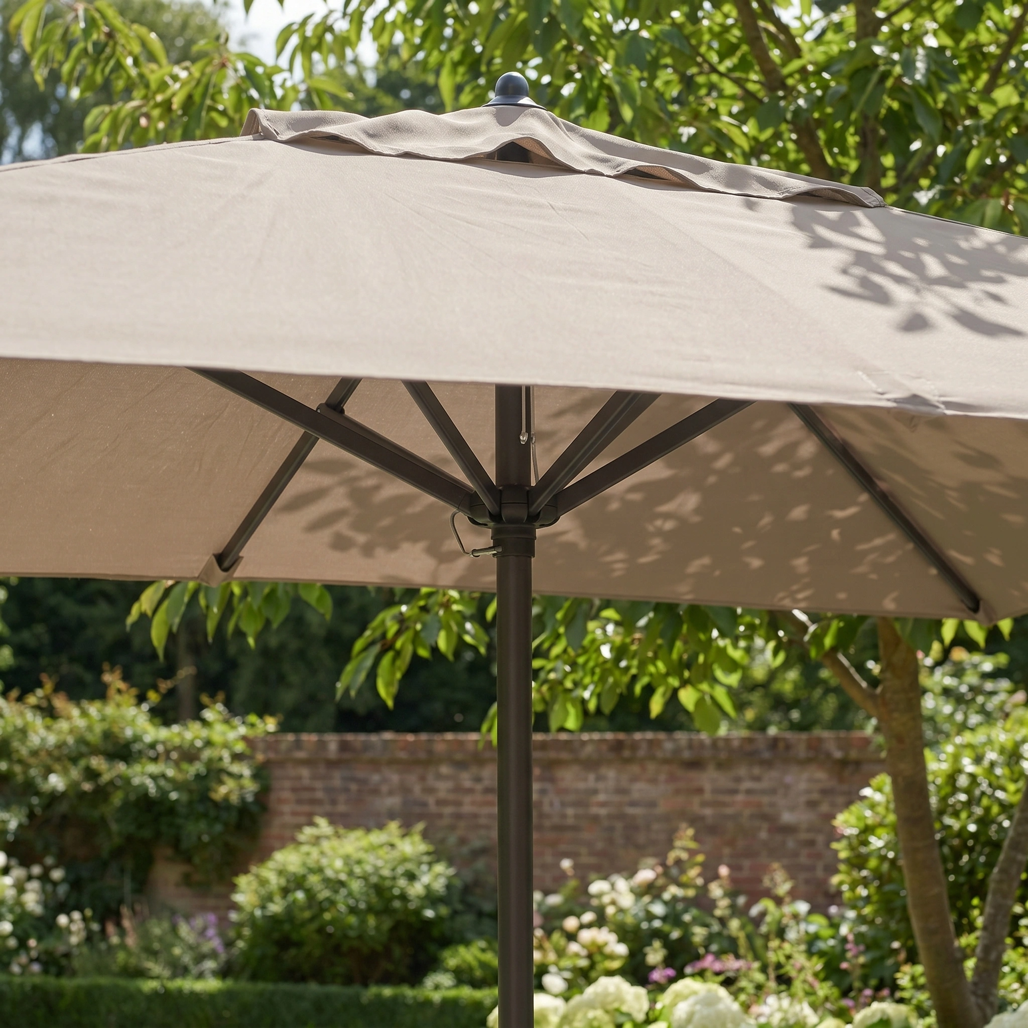 The Triton 3m x 2m Rectangular Aluminium Parasol in Khaki stands open in a garden with trees, flowers, and a brick wall, offering UV protection and fade-resistant outdoor shade.