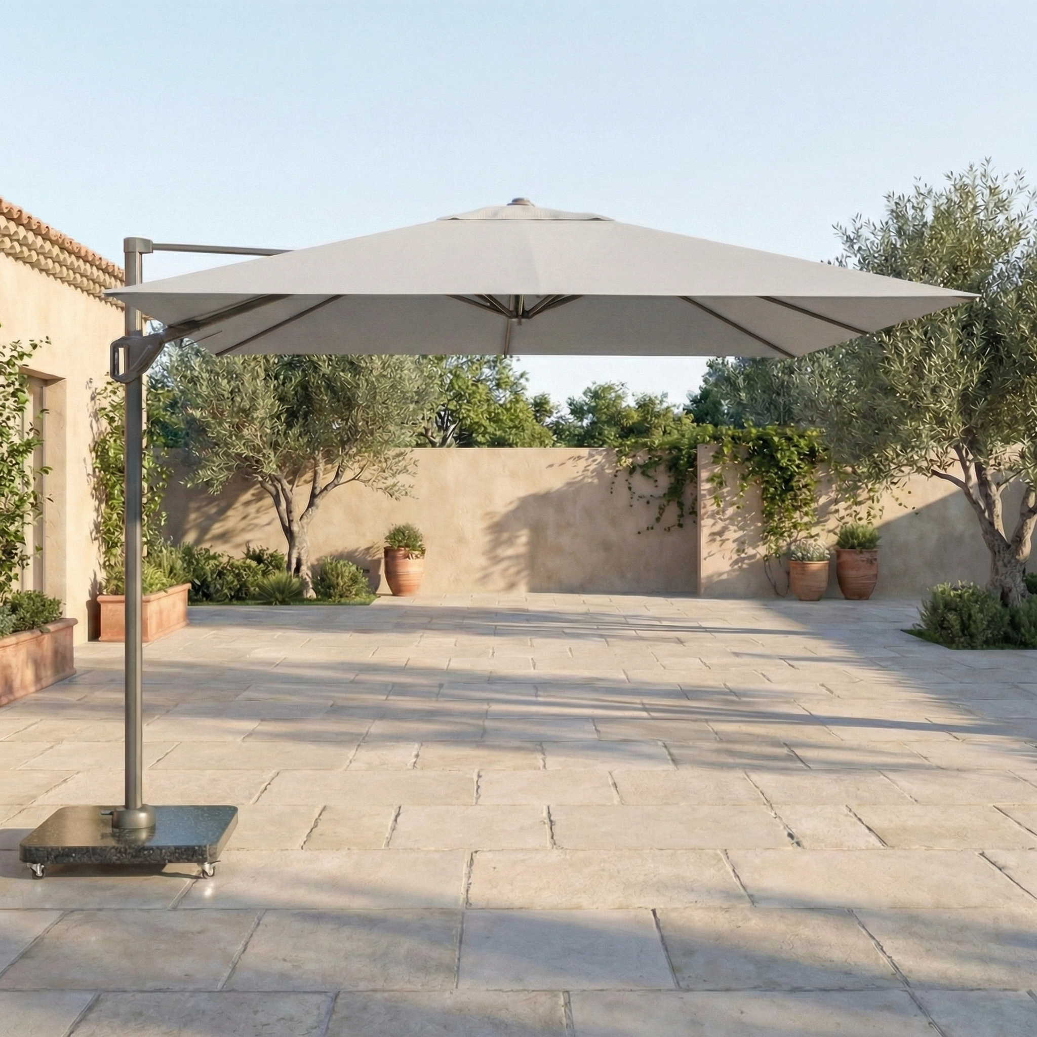 The Voyager T1 3m x 2m Rectangular Cantilever Parasol in Grey with a 90kg Granite Base provides shade on a spacious tiled terrace surrounded by potted plants and trees.
