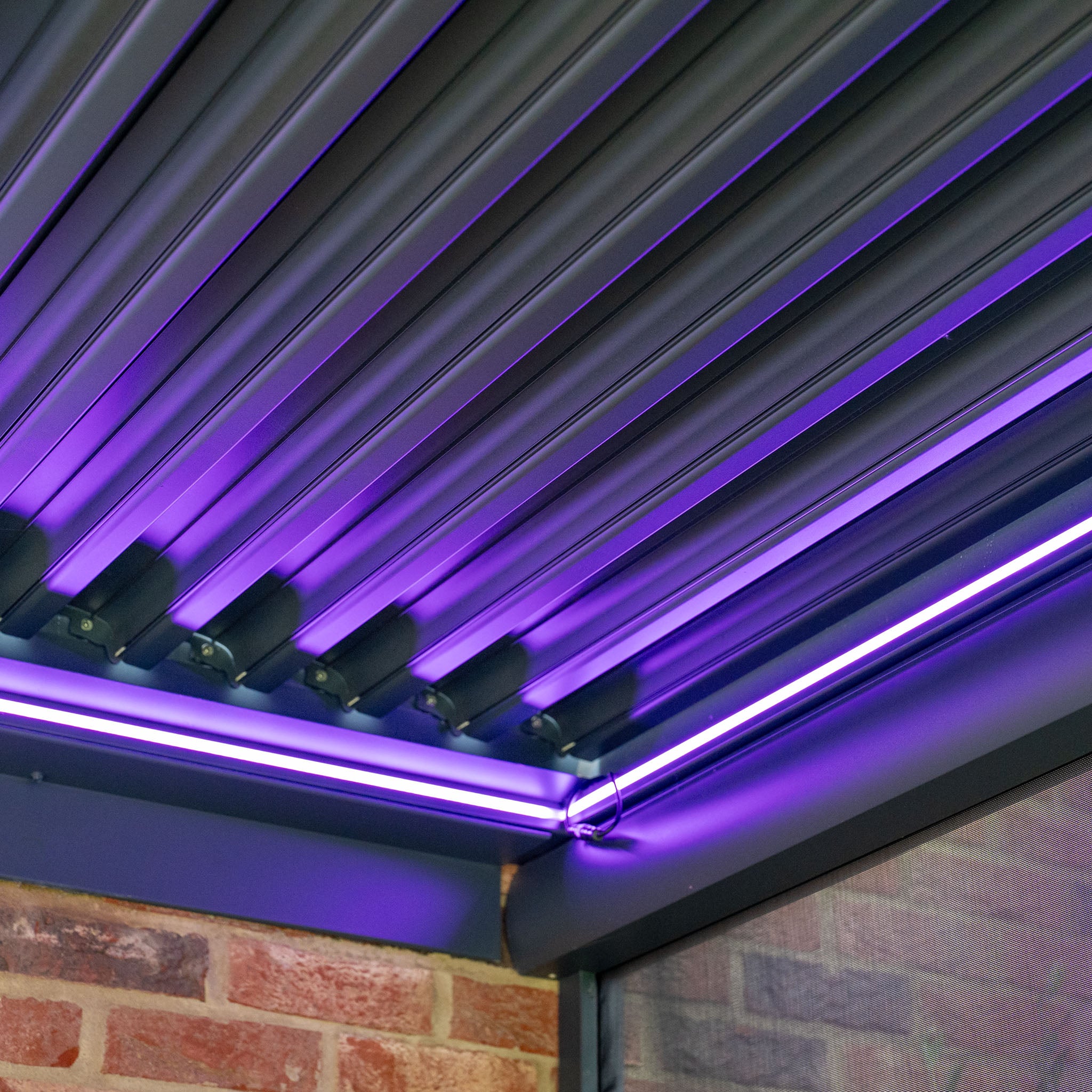 The ceiling, designed like the PergoSTET Plus pergola with angled slats and purple LED lights, casts a vibrant glow over the brick wall corner.