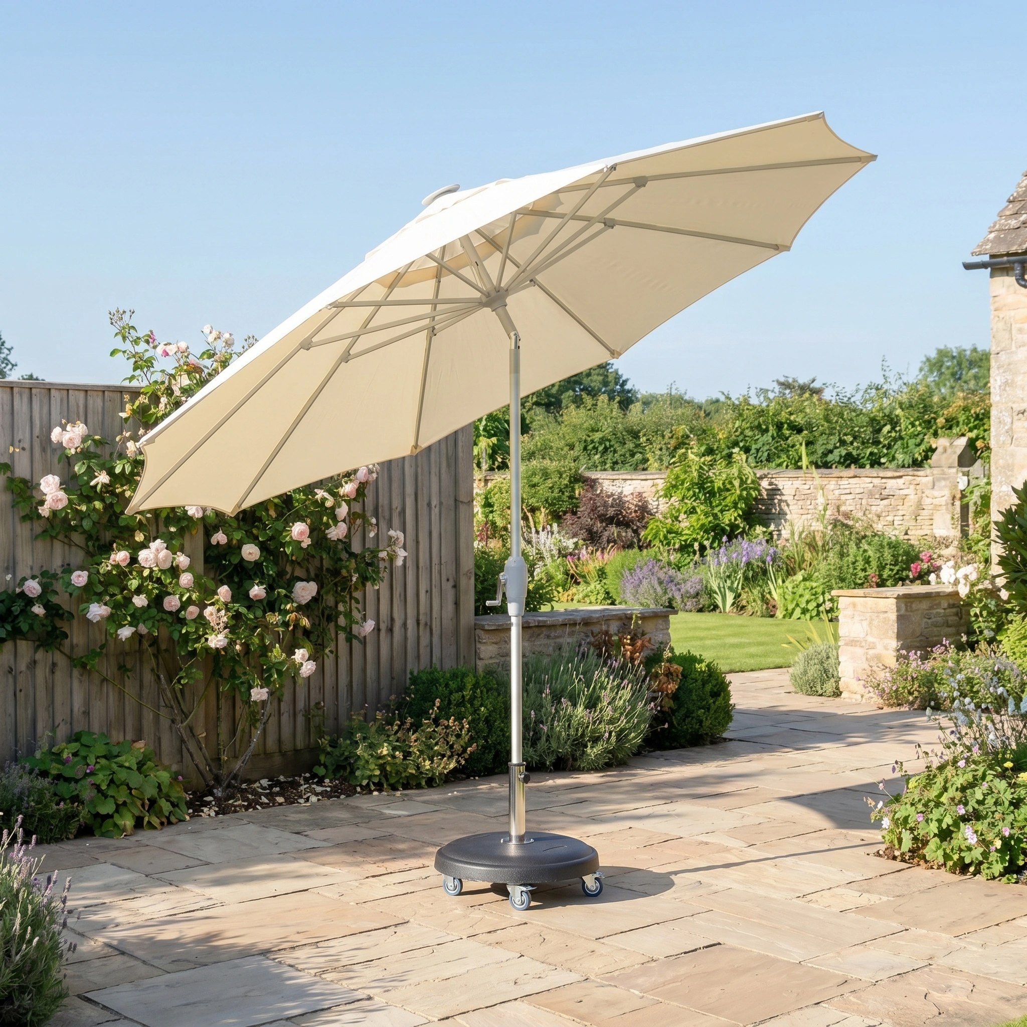 The Zelos 2.5M Round Parasol with LED Lighting in Cream stands on a stone terrace, providing stylish shade and UV protection in a sunny garden.