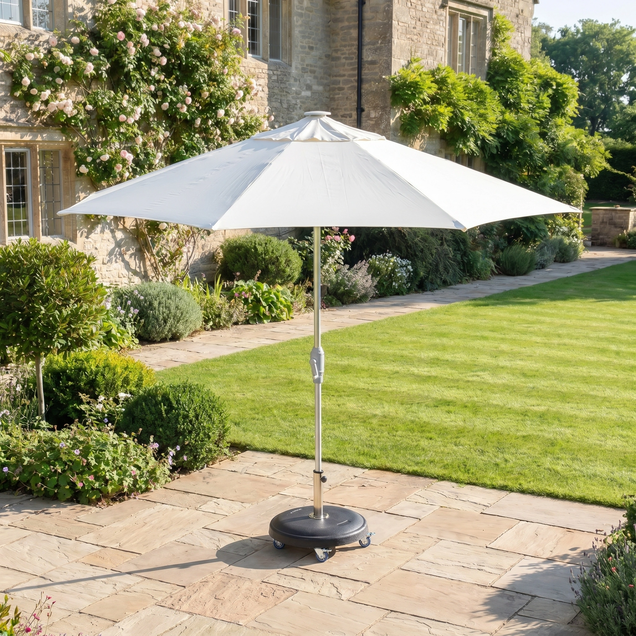 The Zelos 2.5M Round Parasol with LED Lighting in Cream stands on a stone patio, providing sun protection in a sunny, well-kept garden beside a house.