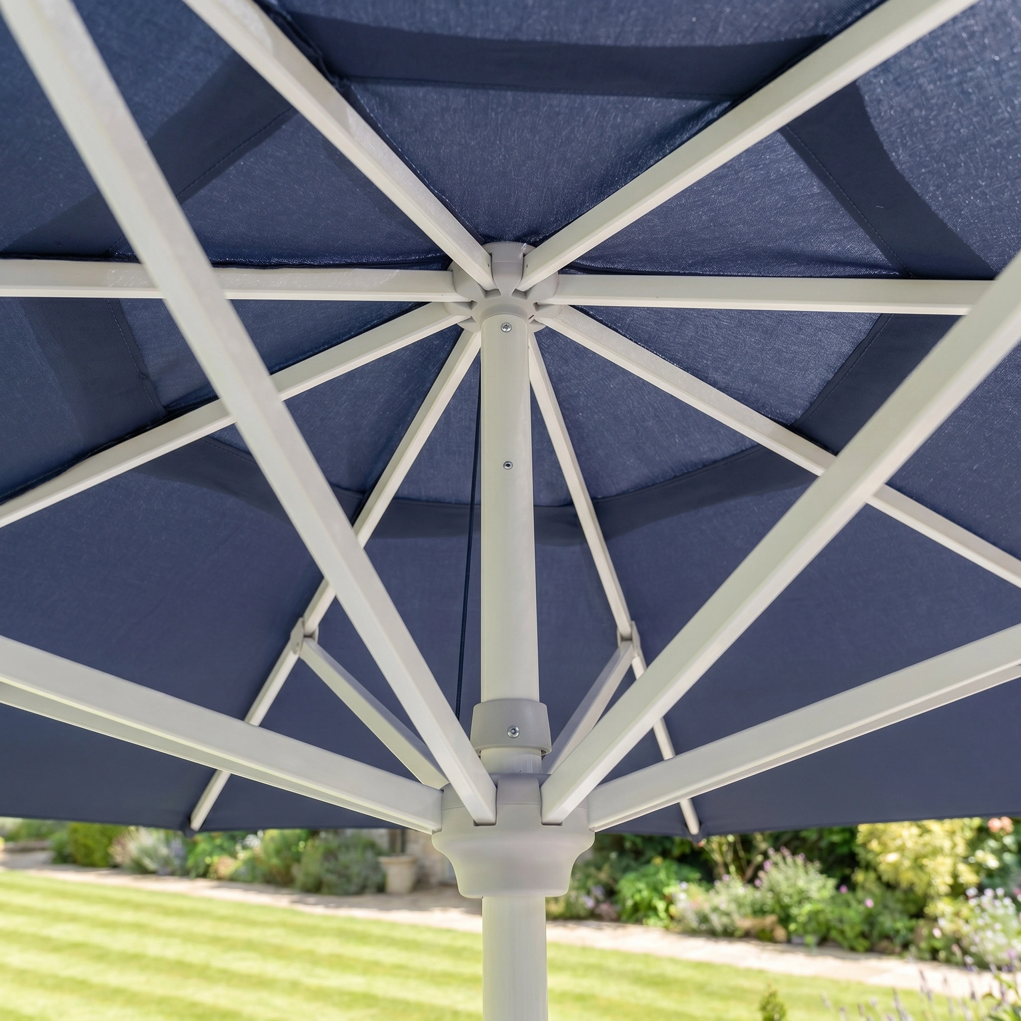 Close-up of the Zelos 2.5M Round Parasol with LED Lighting in Navy, featuring a white frame, shown in a garden setting.