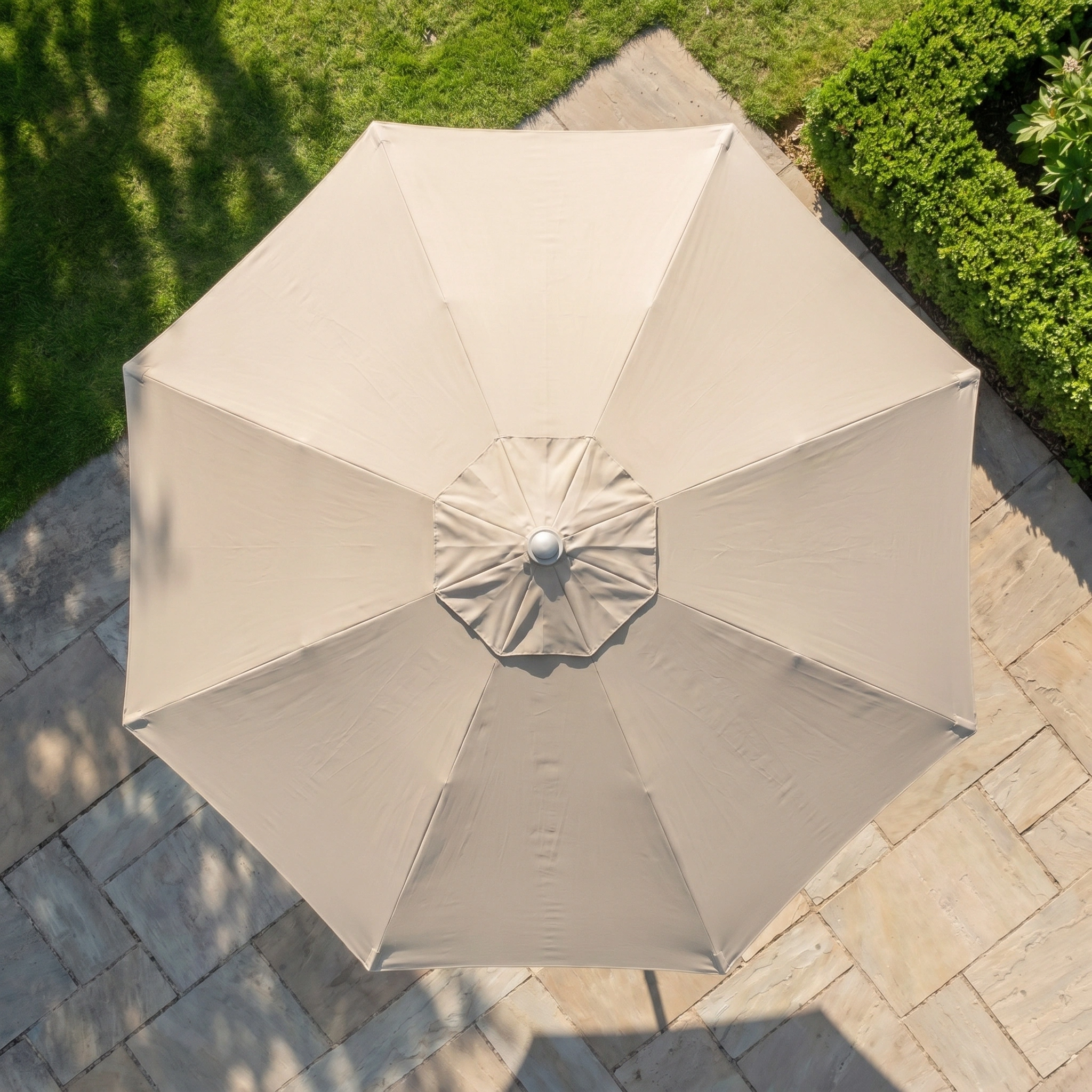 The Zelos 2.5M Round Parasol with LED Lighting in Taupe provides shade over a stone patio and grassy lawn.