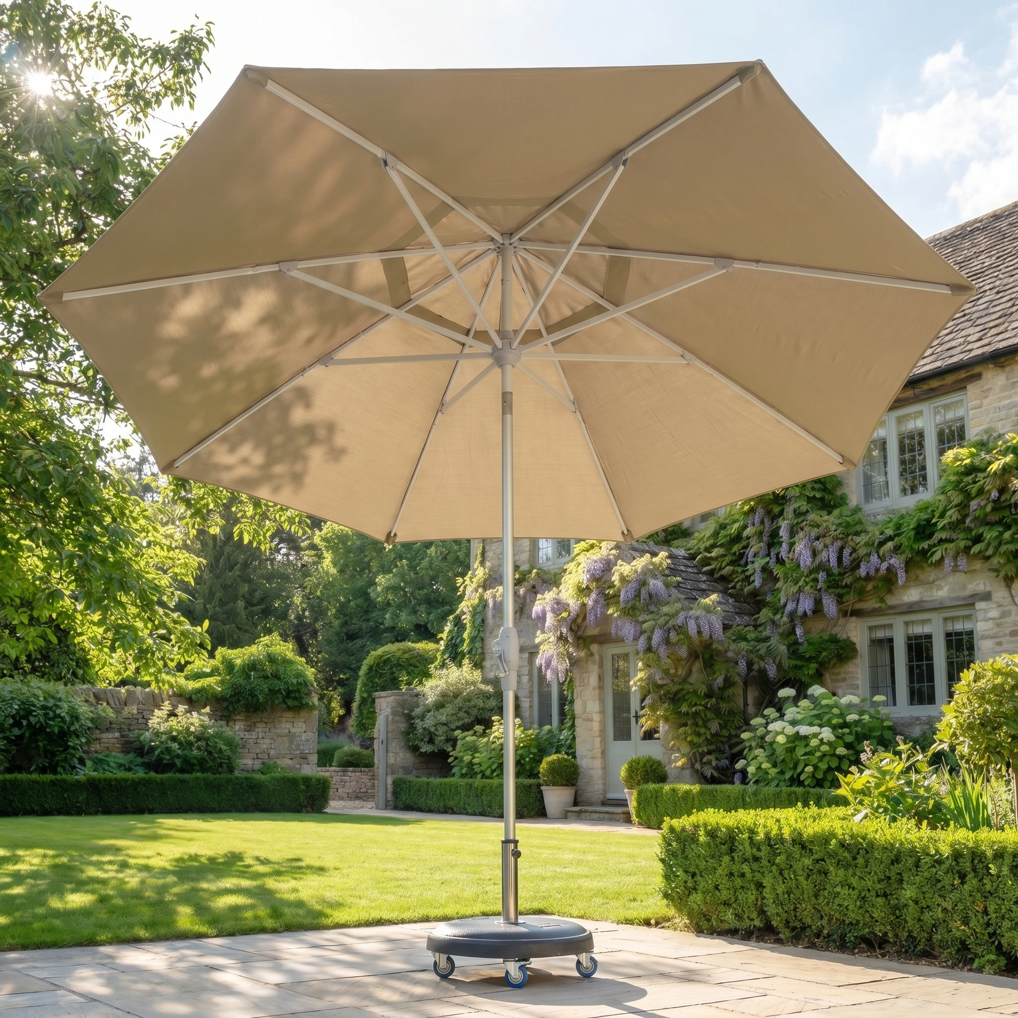 The Zelos 2.5M Round Parasol with LED Lighting in Taupe offers stylish shade and UV protection on a sunny stone terrace in your garden, adding elegance to your outdoor space.