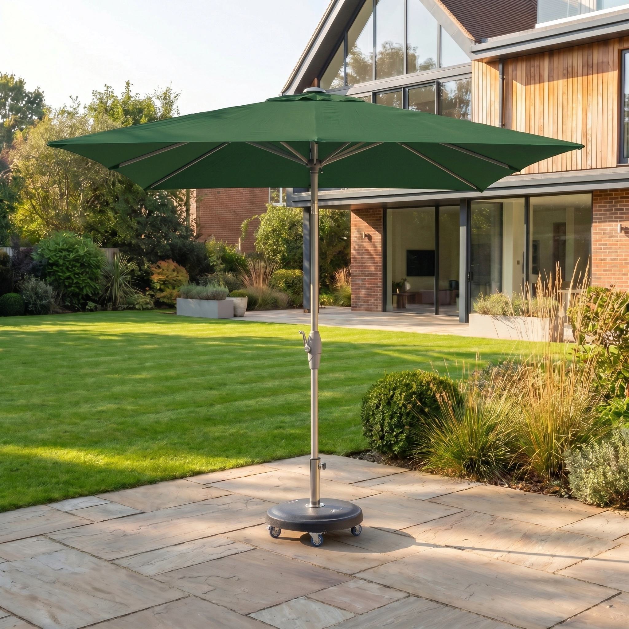 The Zelos 2.5m Square Parasol with LED Lighting in Green provides stylish shade and UV protection for your garden terrace, perfect beside a modern glass-fronted house.
