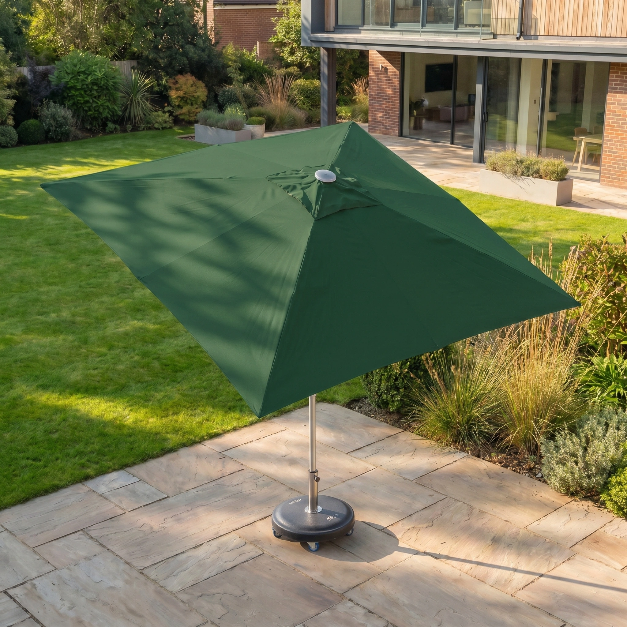 The Zelos 2.5m Square Parasol with LED Lighting in Green offers UV protection, perfect for relaxing on your terrace or garden lawn amid modern greenery and plants.
