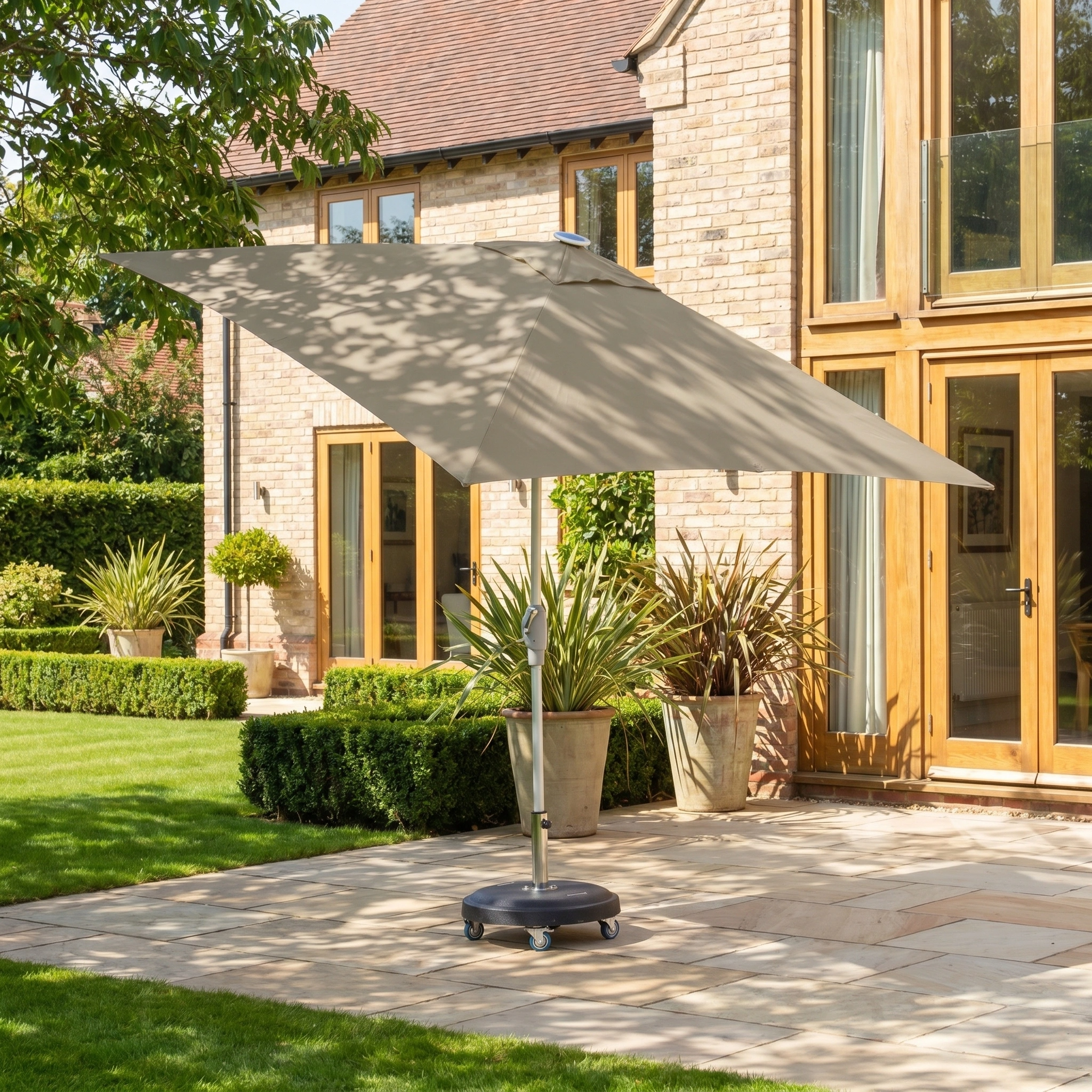 The Zelos 2.5m Square Parasol with LED Lighting in Taupe provides UV protection for relaxing days outdoors, perfect for your backyard stone terrace or garden beside plants and a brick house.